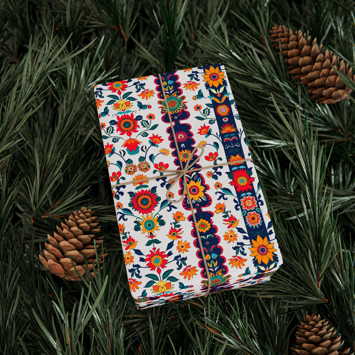 Gift wrapped in red, navy and white folk floral wrapping paper on pine branches with pinecones