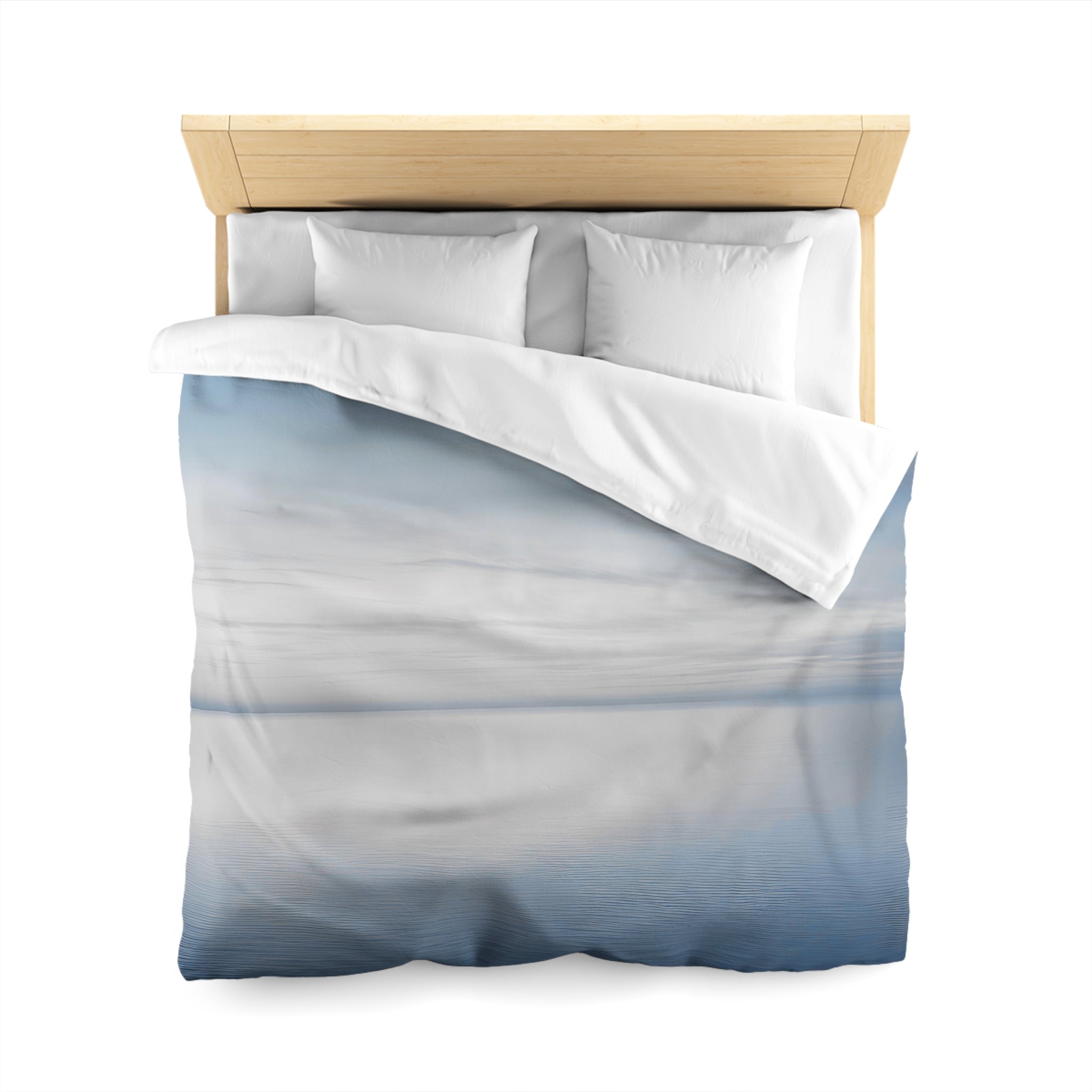 A bed with a white comforter and pillows, featuring a printed design of a cloudy sky or landscape.