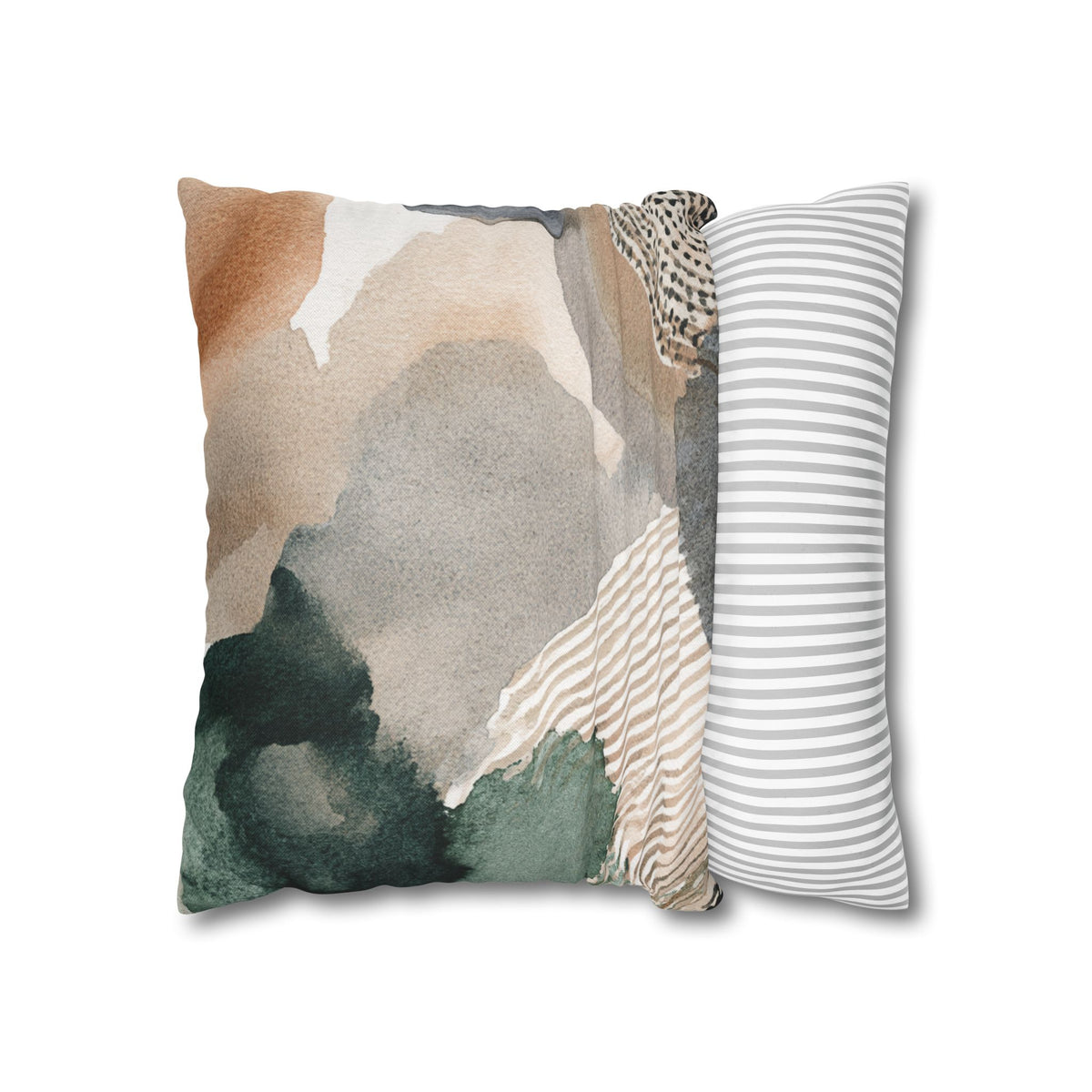 a square pillow with a colorful abstract design, including shades of green, brown, and gray. The pillow is placed on a white surface, and there is a striped pillow to the right of it.
