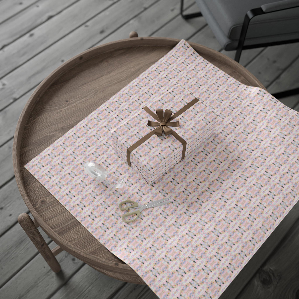 A wooden table with a pink and white patterned wrapping paper, a pair of scissors, and a small gift box on top.