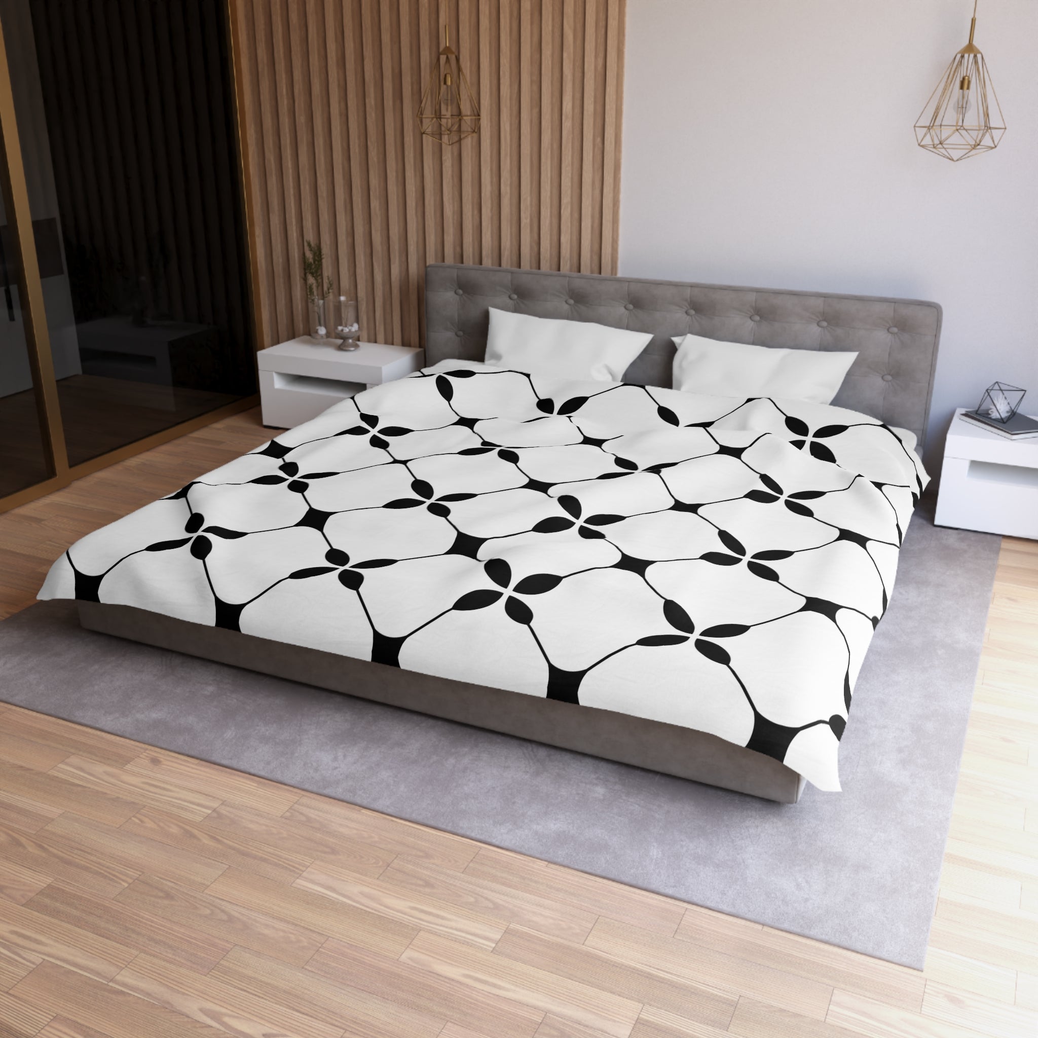 a modern bedroom with a large bed, a gray headboard, and a black and white patterned comforter. The room has a wooden floor and white walls, creating a clean and minimalist aesthetic.
