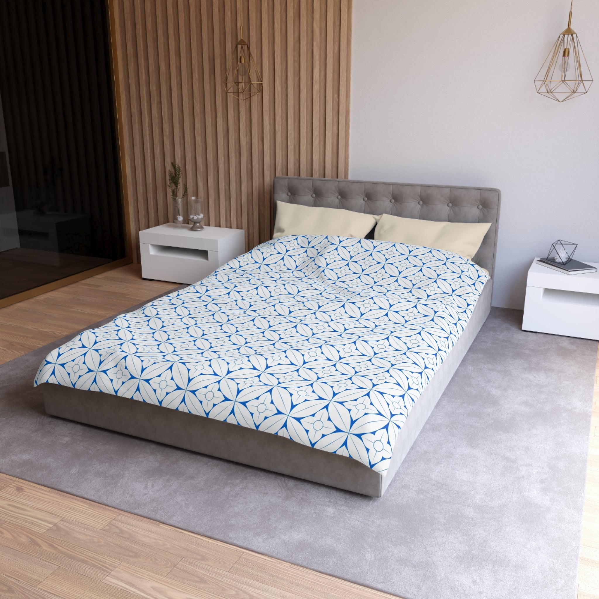 a modern bedroom with a gray tufted headboard, a white bedside table, and a gray area rug. The bed is covered in a blue and white patterned comforter, and there are two white pillows on the bed.