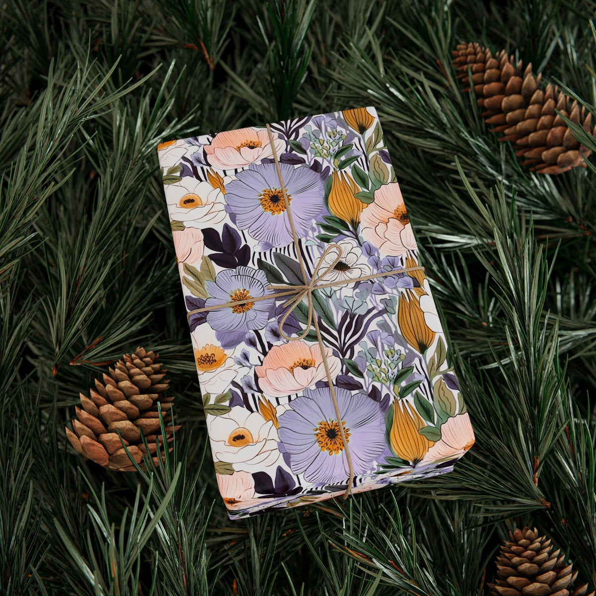 Gift wrapped in lilac and peach garden blossom wrapping paper on pine branches with pinecones
