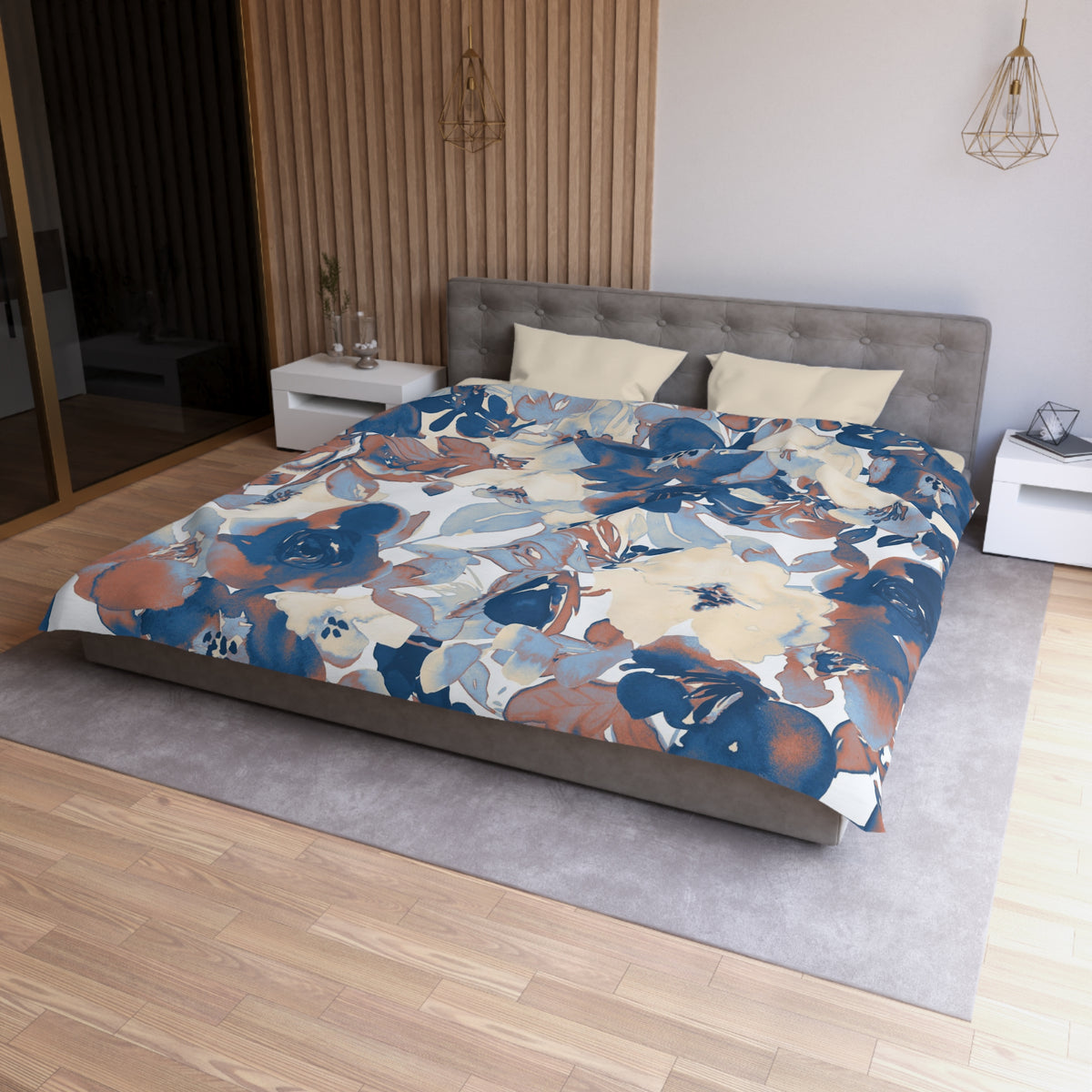 a modern bedroom with a large bed covered in a floral print comforter. The bed is positioned against a wall with a wooden panel. The room has a gray headboard and a white nightstand on each side of the bed. The floor is covered with a gray rug.