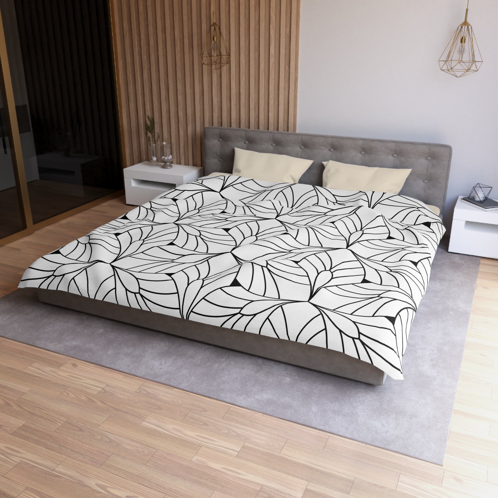 a modern bedroom with a large bed, a gray headboard, and a black and white leaf-patterned comforter. The room has a wooden floor and white walls, creating a clean and minimalist aesthetic.