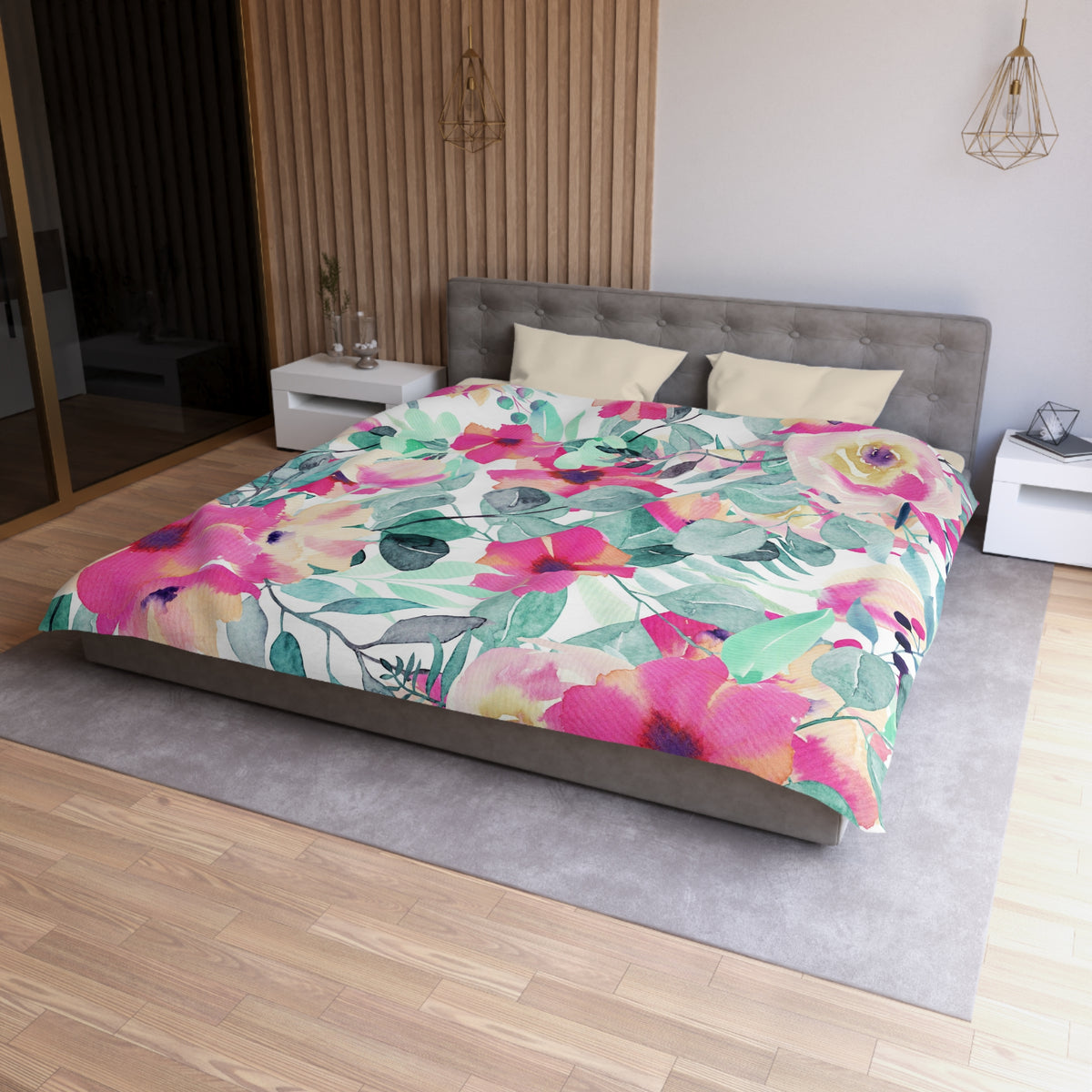 a modern bedroom with a large bed covered in a colorful floral comforter. The bed is positioned against a wall with a wooden panel. The room has a gray headboard and a white nightstand on each side of the bed. There is also a pendant light hanging above the bed.