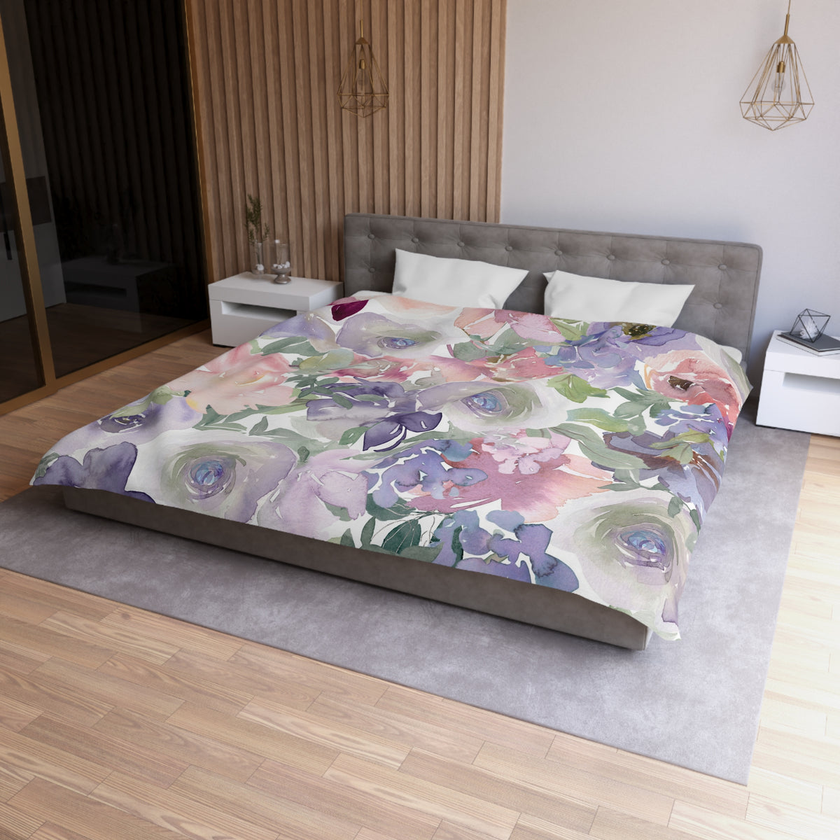 a bedroom with a large bed covered in a colorful floral comforter. The bed is positioned against a wall with a wooden panel. The room has a modern and minimalist design, with a gray headboard and white nightstands. There is also a pendant light hanging above the bed.
