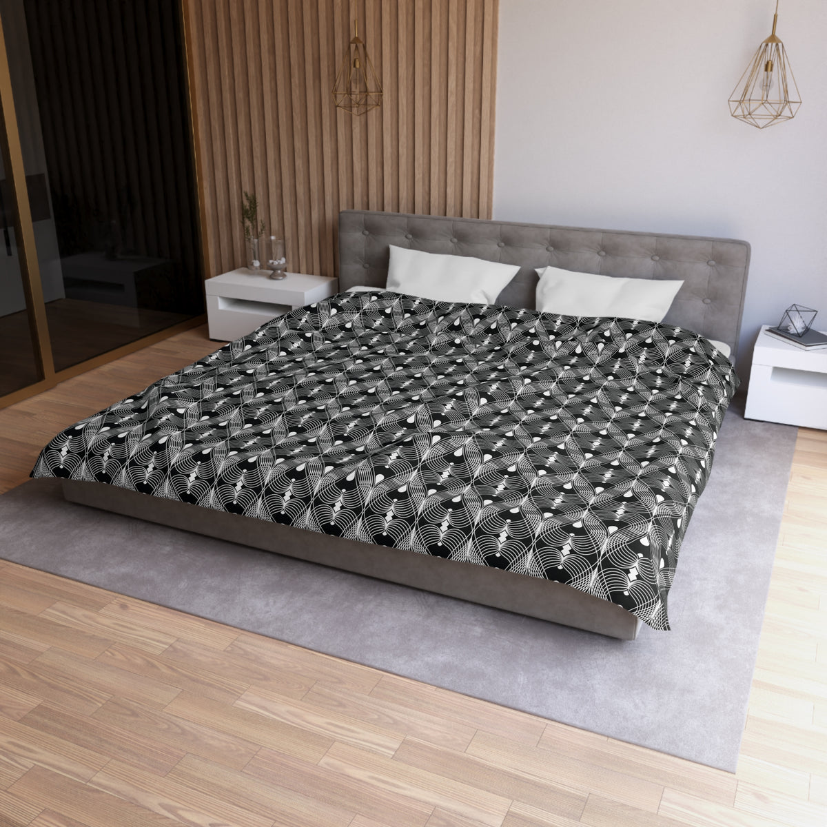 a modern bedroom with a large bed, a gray headboard, and a black and white patterned comforter. The room has a wooden floor and white walls, creating a clean and minimalist aesthetic.
