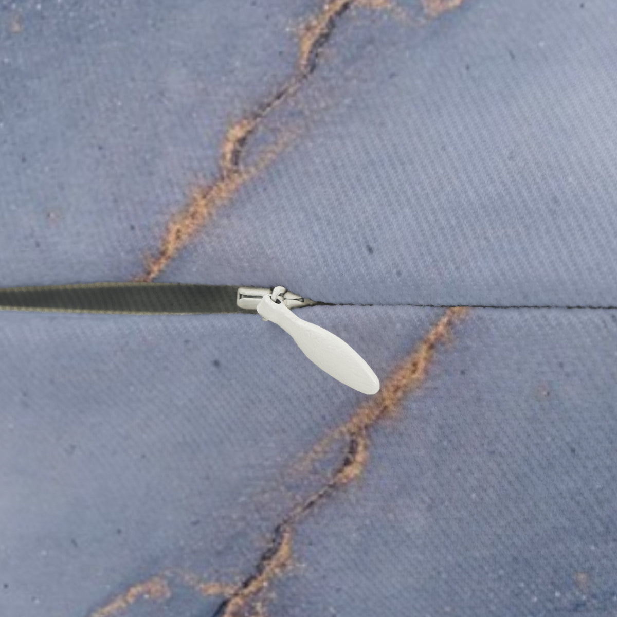 A close-up view of a zipper on a piece of fabric, with a white plastic handle visible.