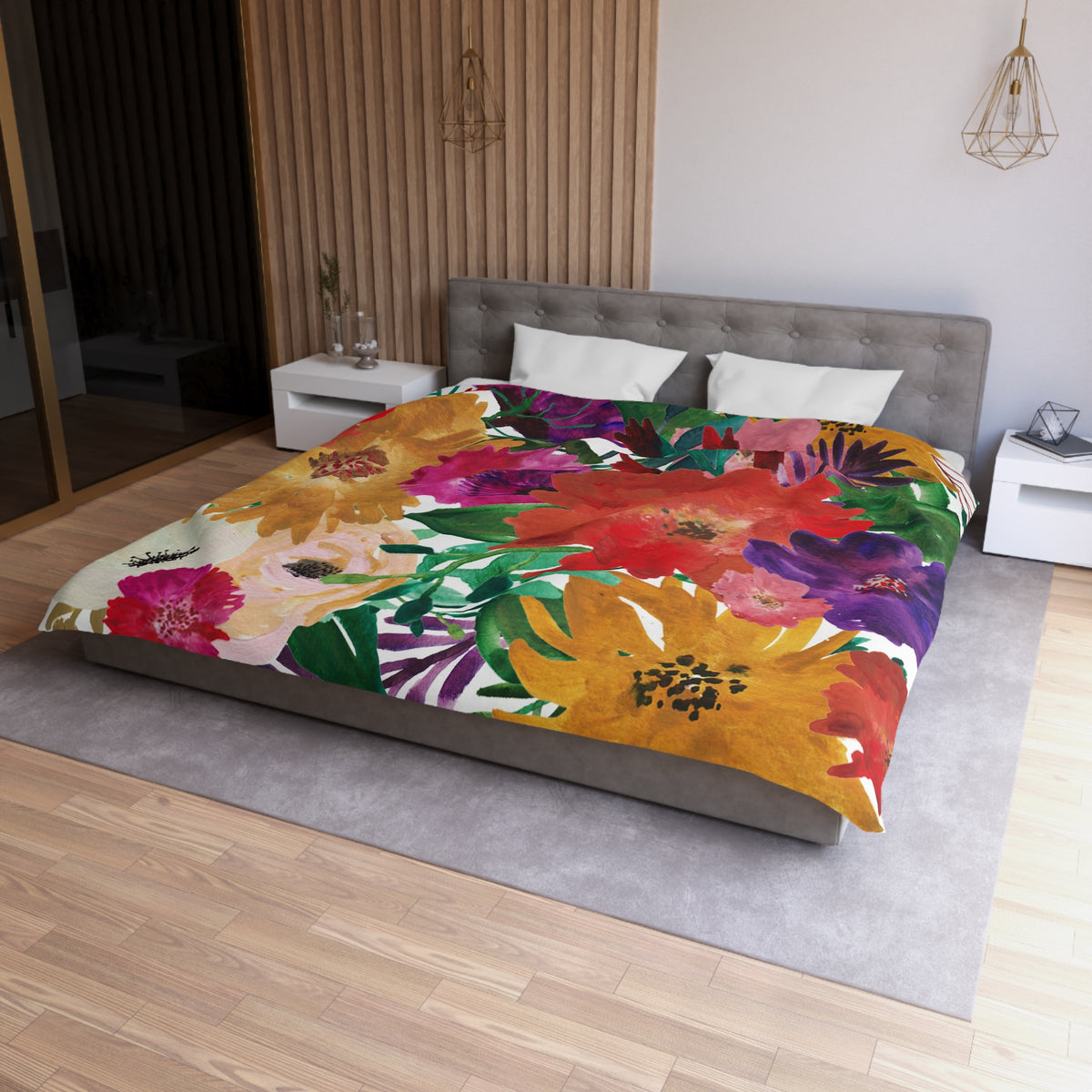 a modern bedroom with a large bed covered in a colorful floral comforter. The bed is positioned against a wall with a wooden panel. The room has a minimalist design, with white walls and a gray floor. There are two nightstands on either side of the bed, and a pendant light hangs above the bed.