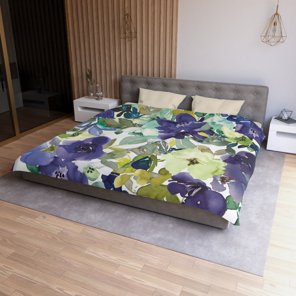 a bedroom with a large bed covered in a colorful floral comforter. The bed is positioned against a wall with a wooden panel. The room has a modern and minimalist design, with a gray headboard and white nightstands.