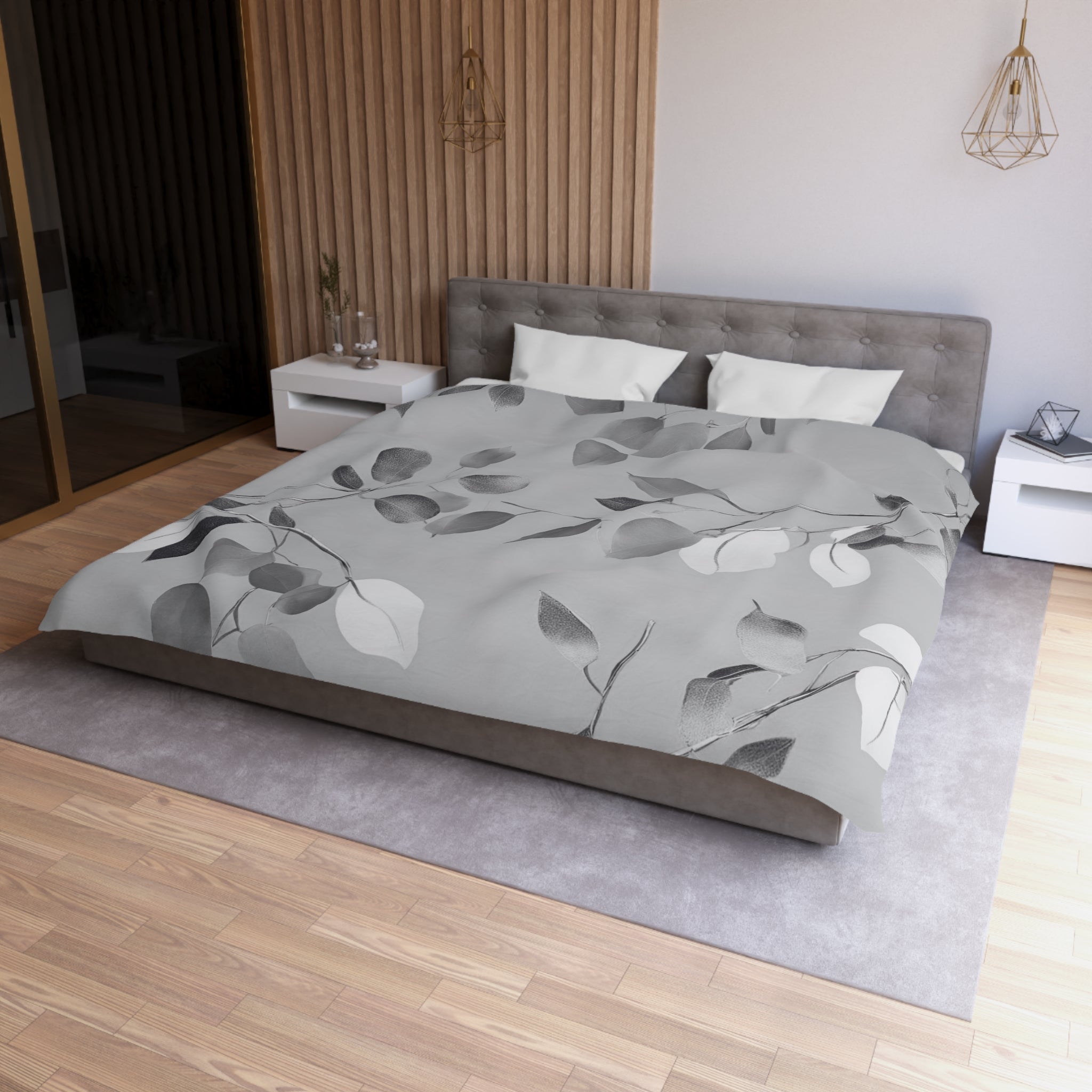 a modern bedroom with a large bed, a gray headboard, and a gray and white leaf-patterned comforter. The room has a wooden floor and white walls, creating a serene and minimalist atmosphere.