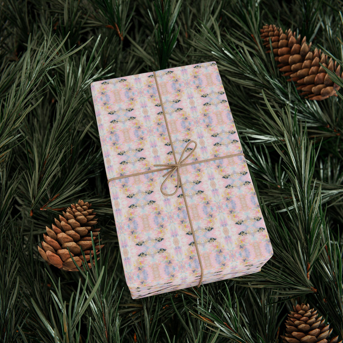A gift box with a patterned wrapping paper is placed on top of pine needles and pine cones, creating a festive and natural setting.