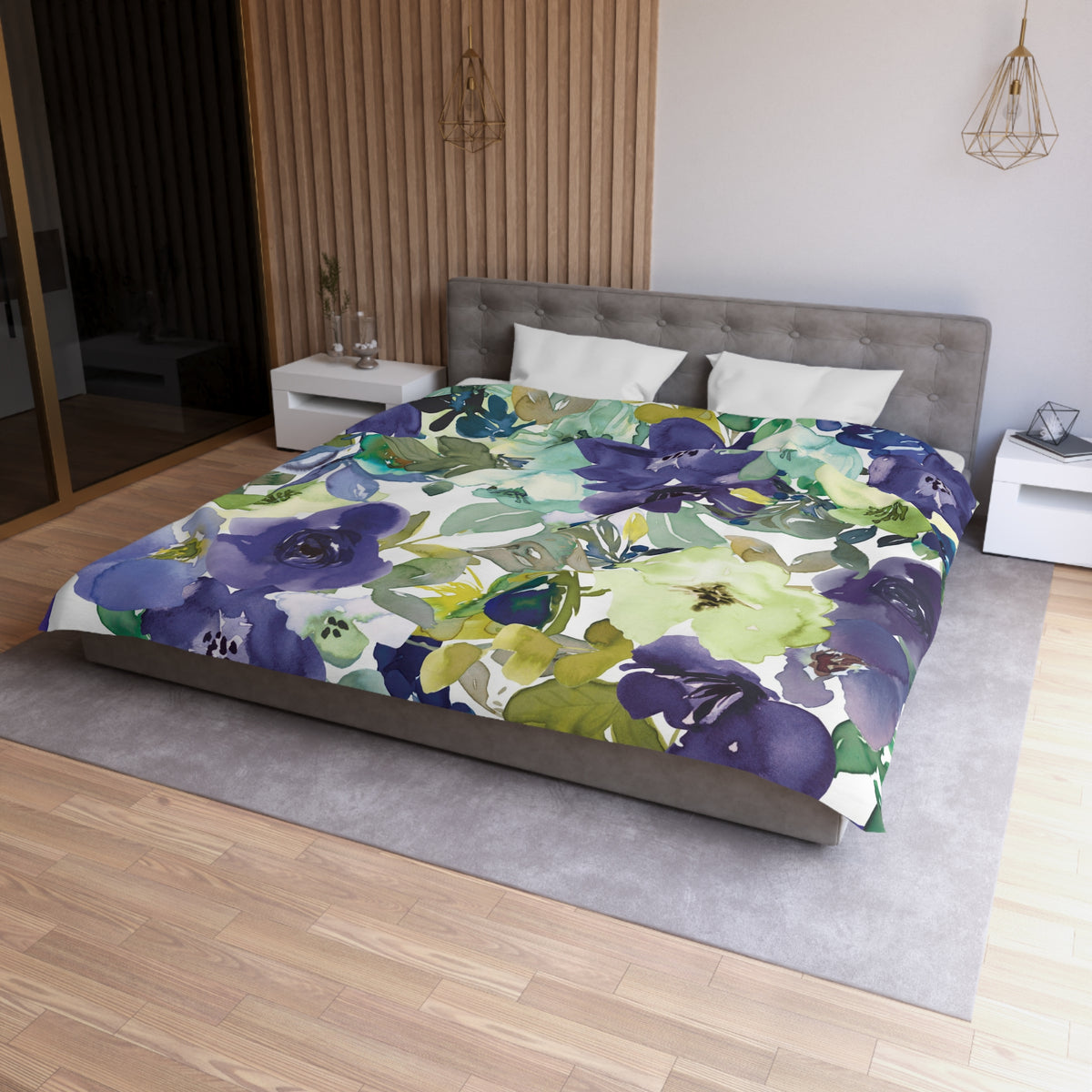 a bedroom with a large bed covered in a colorful floral comforter. The bed is positioned against a wall with a wooden panel. The room has a modern and minimalist design, with a gray headboard and white nightstands.