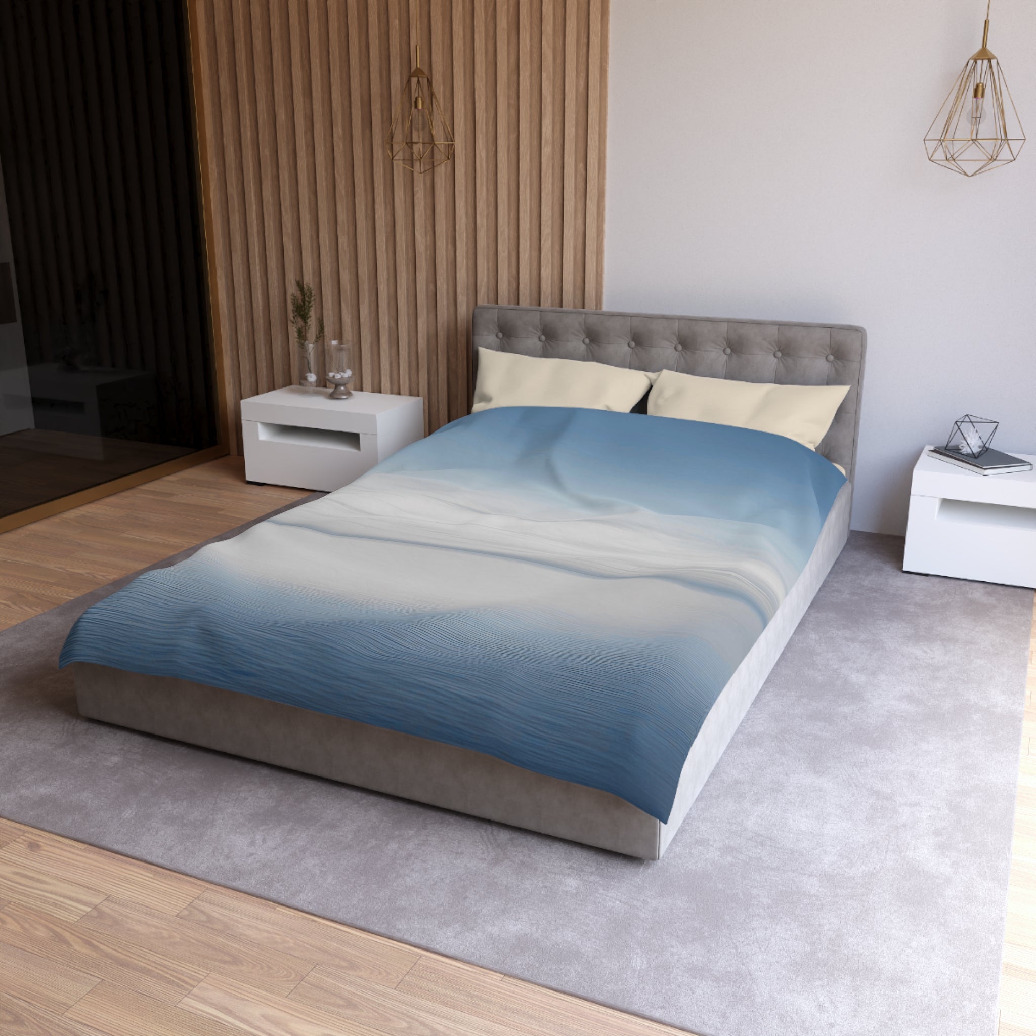a modern bedroom with a gray tufted headboard, a blue and white gradient comforter, and a white nightstand on the left side. The room has a wooden floor and a gray area rug, creating a cozy and stylish atmosphere.