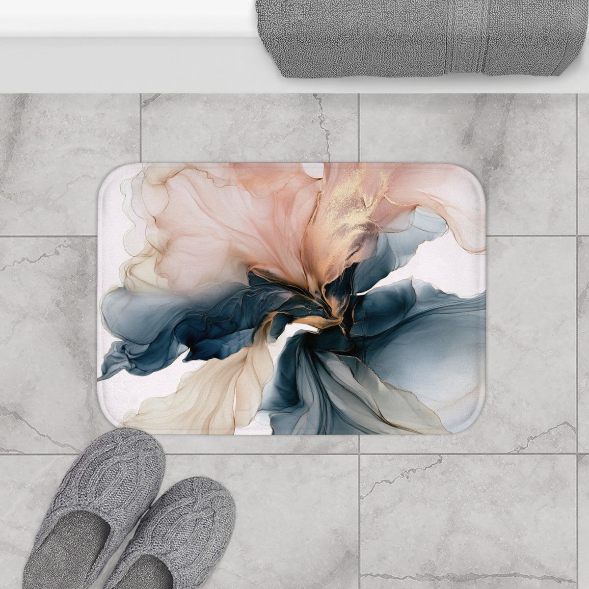 a bathroom floor with a decorative floral pattern on the floor mat, gray slippers placed next to it, and a rolled-up towel on the countertop.