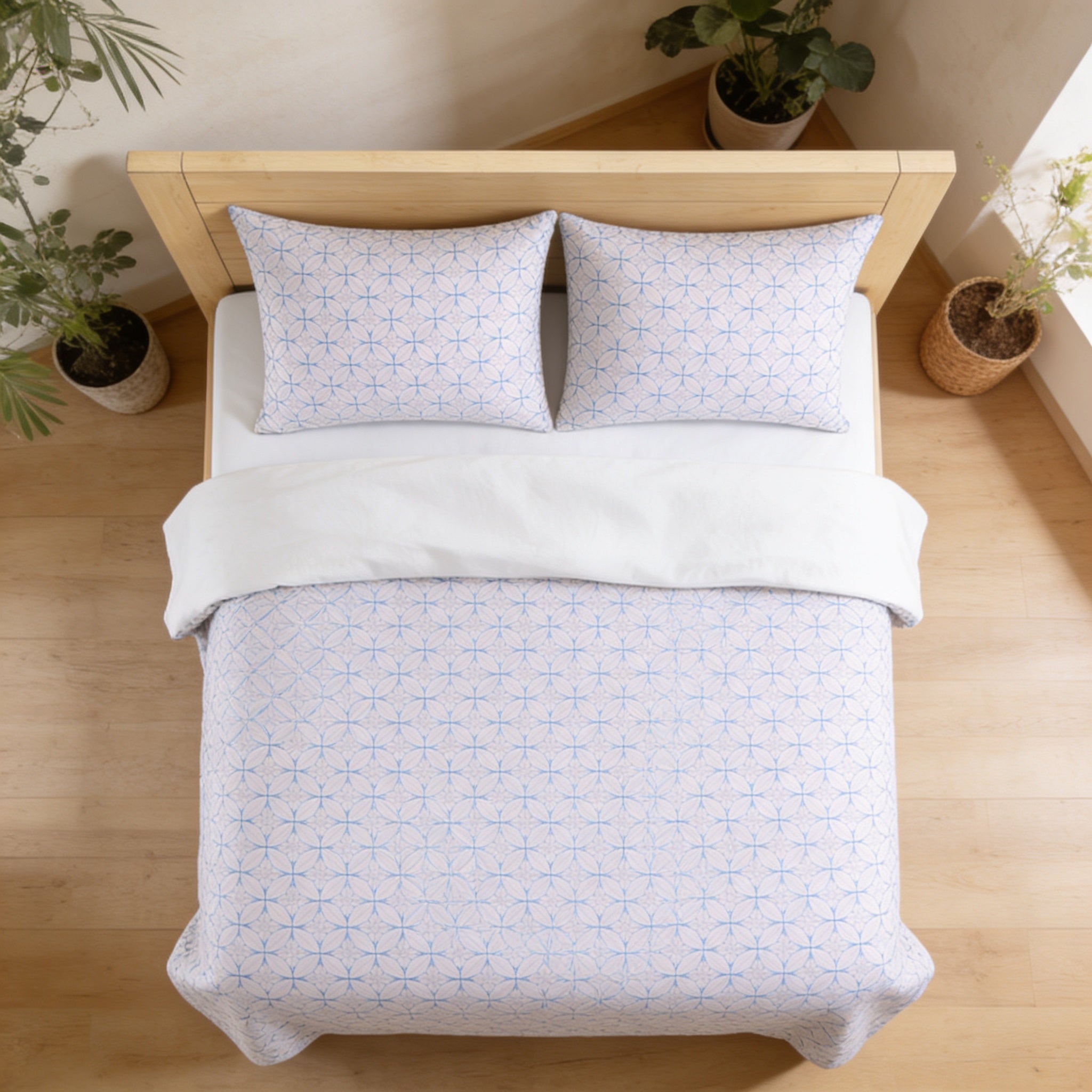a neatly made bed with a white comforter and matching pillows, set against a backdrop of a wooden headboard and two potted plants.