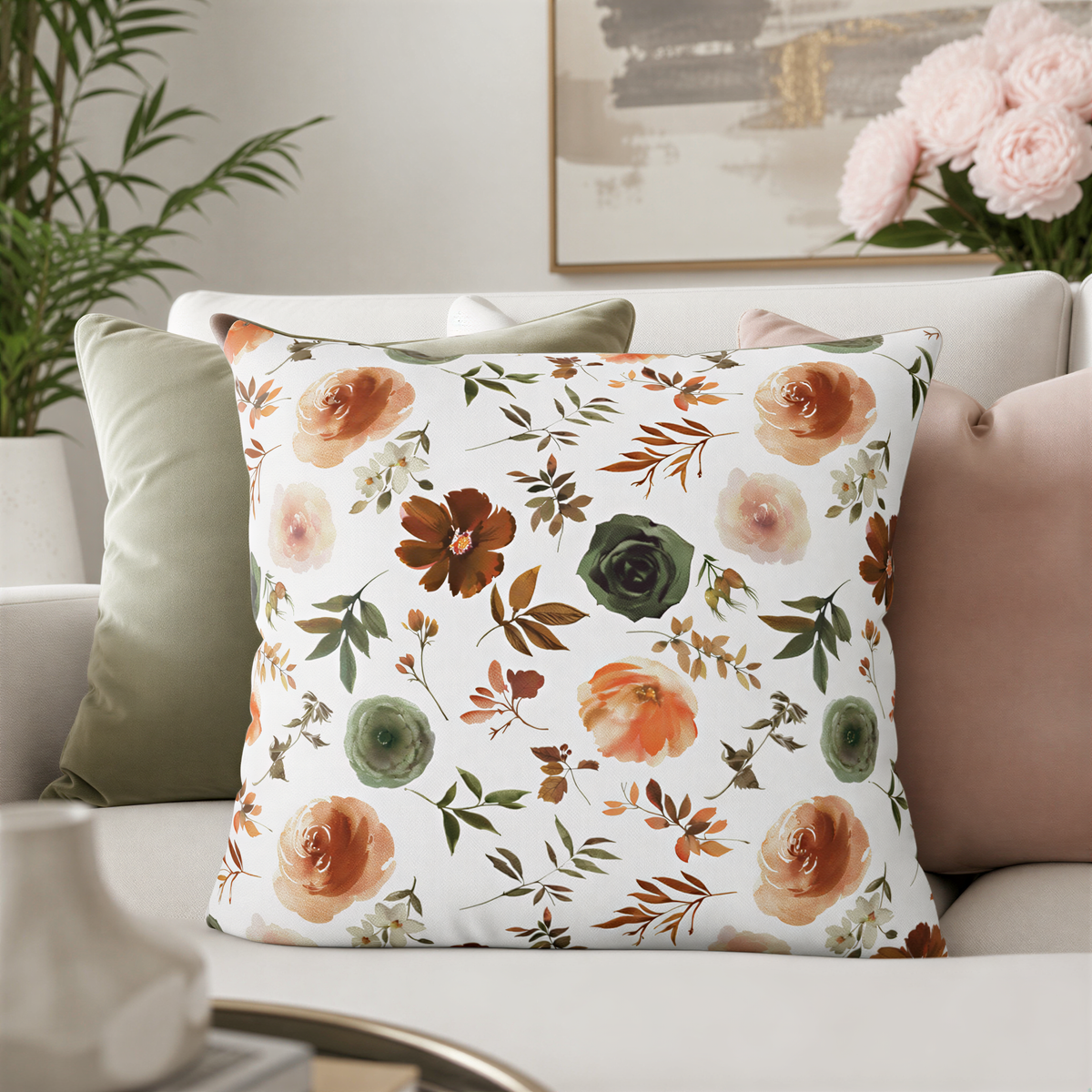 a living room with a white sofa adorned with a floral throw pillow. The pillow has a vibrant floral pattern in shades of orange, green, and brown, creating a warm and inviting atmosphere. In the background, there is a painting and a potted plant, adding to the cozy and welcoming ambiance of the space.