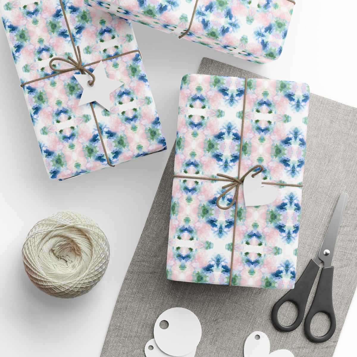Blush, blue and green mirrored watercolor wrapping paper on gifts tied with twine, with gift tags and scissors