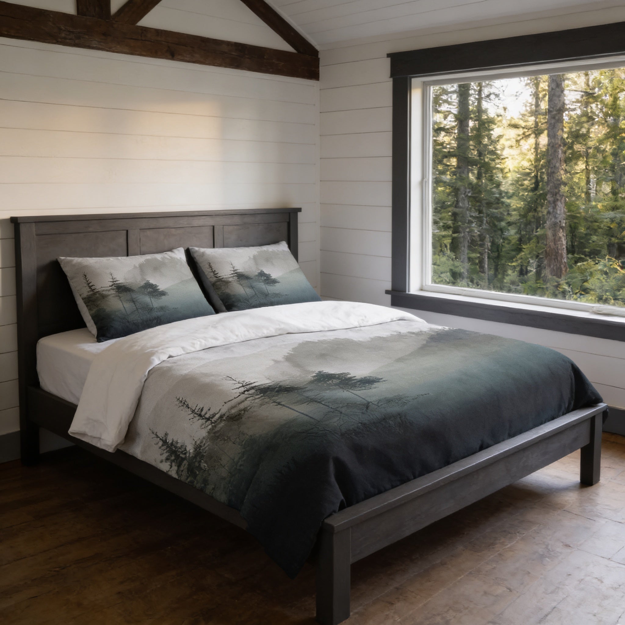 a serene bedroom scene with a bed featuring a gray and white forest-themed comforter and pillows, set against a backdrop of a large window overlooking a wooded area.