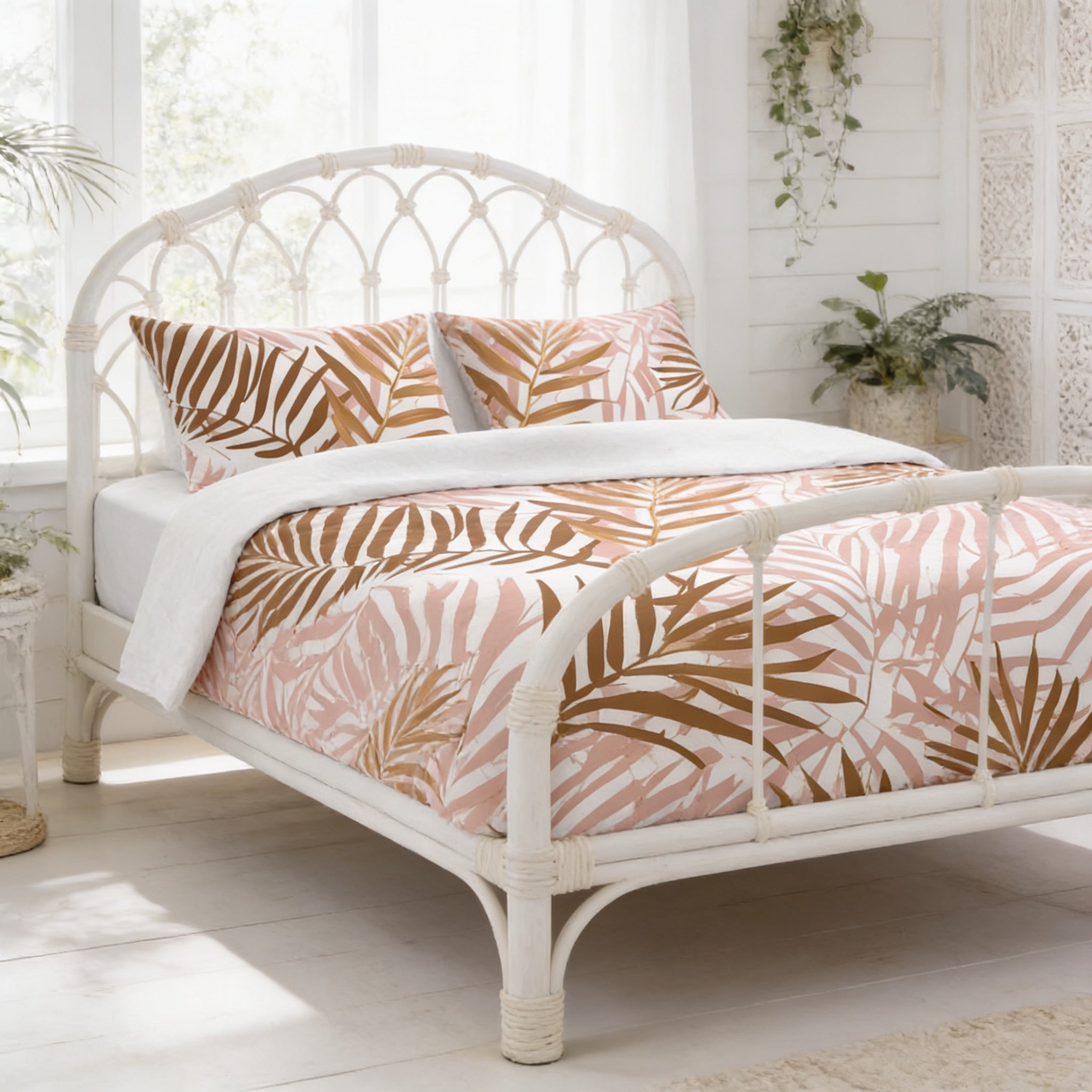 a white bed with a tropical leaf patterned comforter and pillows, set against a white background with a window and plants.
