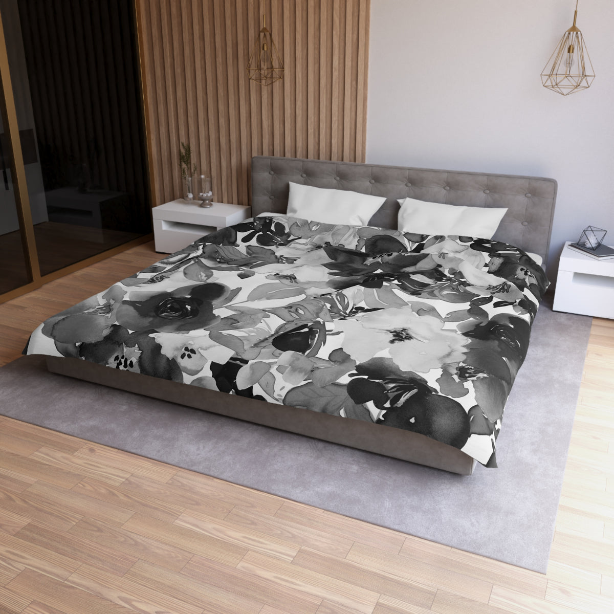 a modern bedroom with a large bed covered in a black and white floral comforter. The bed is positioned against a wall with a wooden panel. The room also features a nightstand, a pendant light, and a rug on the floor.