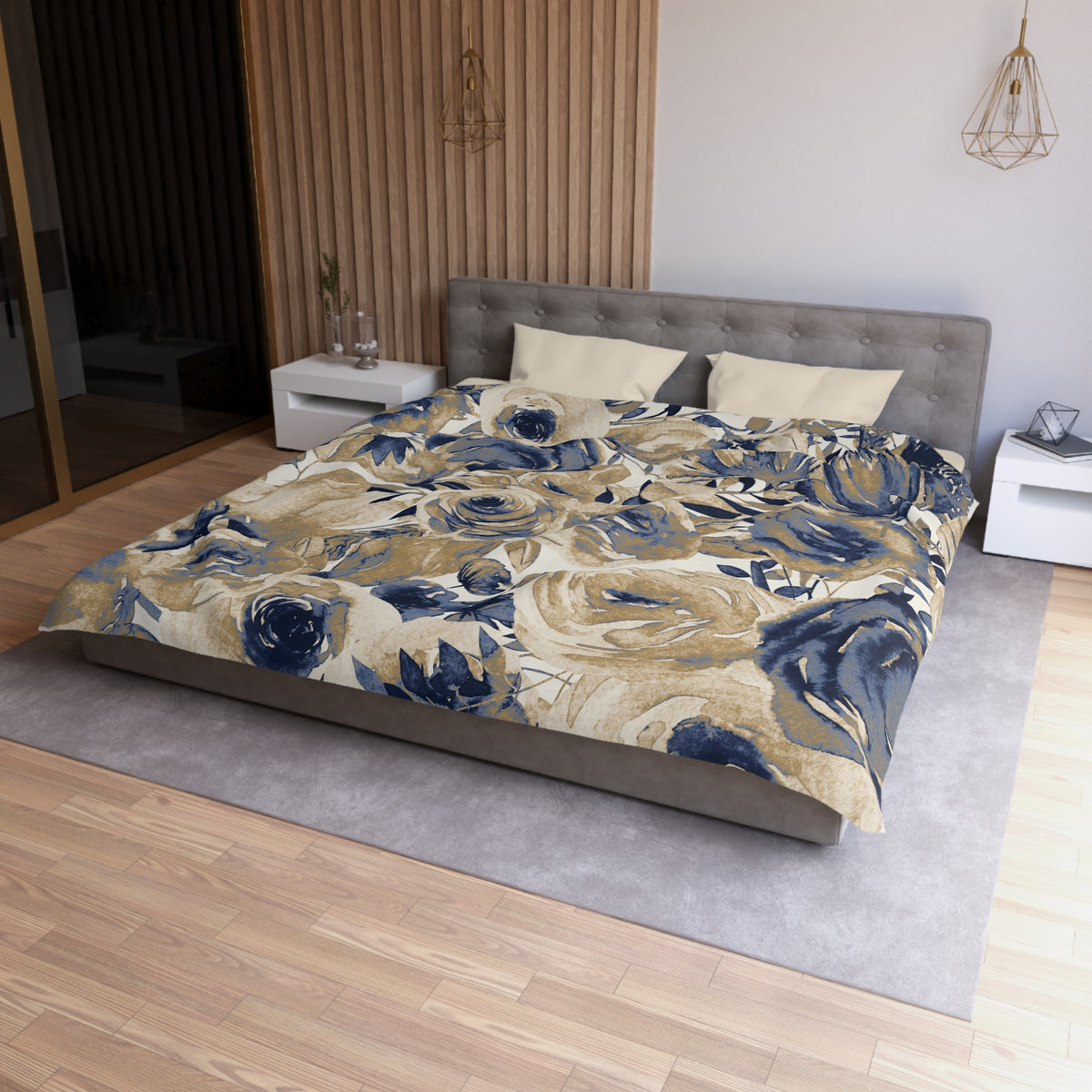 a modern bedroom with a large bed covered in a floral print comforter. The bed is positioned against a wall with a wooden panel. The room has a gray headboard and a white nightstand on each side of the bed. There is also a pendant light hanging above the bed.