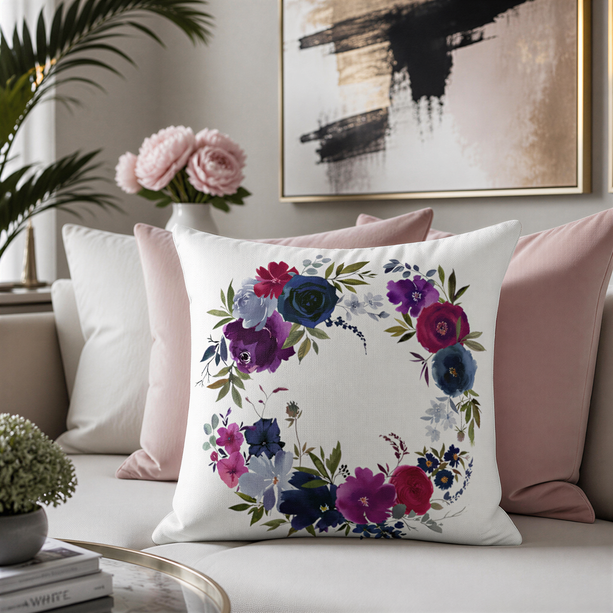a living room with a white sofa adorned with colorful throw pillows. A large floral wreath pillow is prominently displayed on the sofa, adding a touch of elegance and natural beauty to the space. In the background, there are two potted plants, one on the left side and the other on the right side of the sofa, further enhancing the room's ambiance. A framed picture hangs on the wall, completing the cozy and inviting atmosphere of the living room.