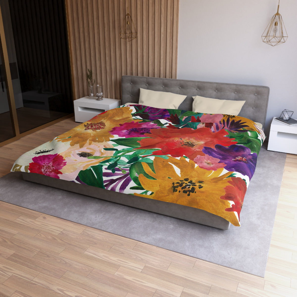 a modern bedroom with a large bed covered in a colorful floral comforter. The bed is positioned against a wall with a wooden panel. The room has a minimalist design, with white walls and a gray floor. There are two nightstands on either side of the bed, and a pendant light hangs above the bed.