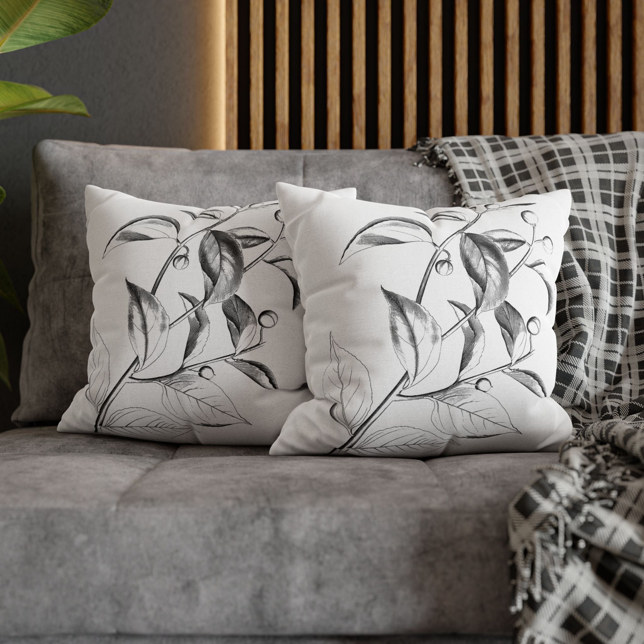 a gray couch with two white throw pillows featuring black leaf designs. The pillows are placed on the couch, creating a cozy and inviting atmosphere.