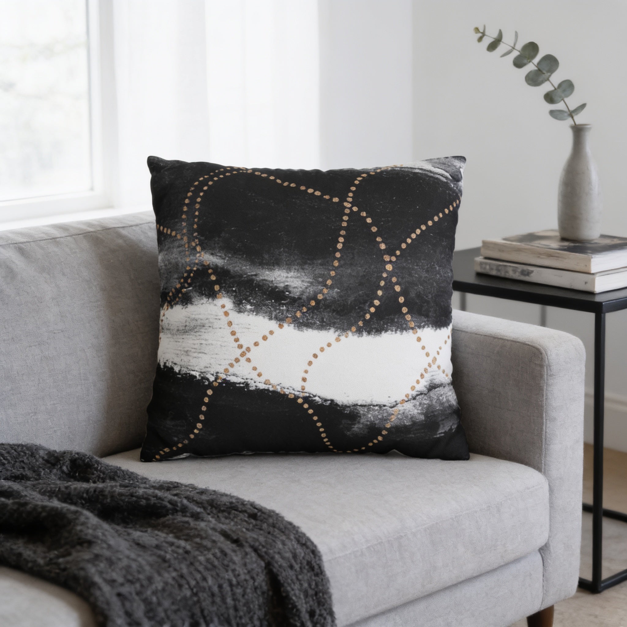 a gray sofa with a black and white throw pillow on it, and a small side table with a vase of greenery on top.