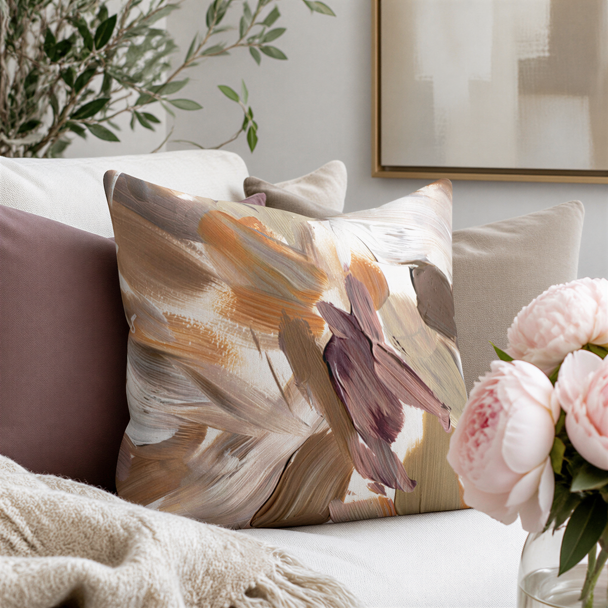 a cozy living room with a large, colorful throw pillow on a couch, a vase of pink flowers, and a painting on the wall.