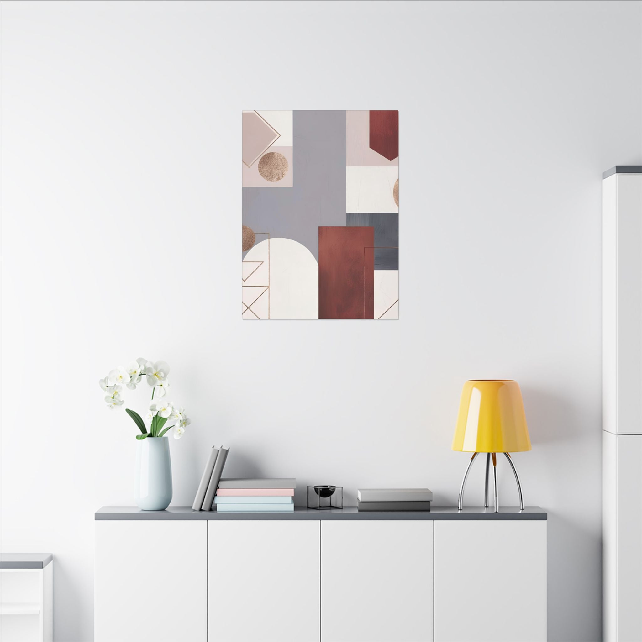 a minimalist living space with a white wall, a white cabinet, a yellow lamp, a vase with white flowers, and a framed abstract art piece above the cabinet.