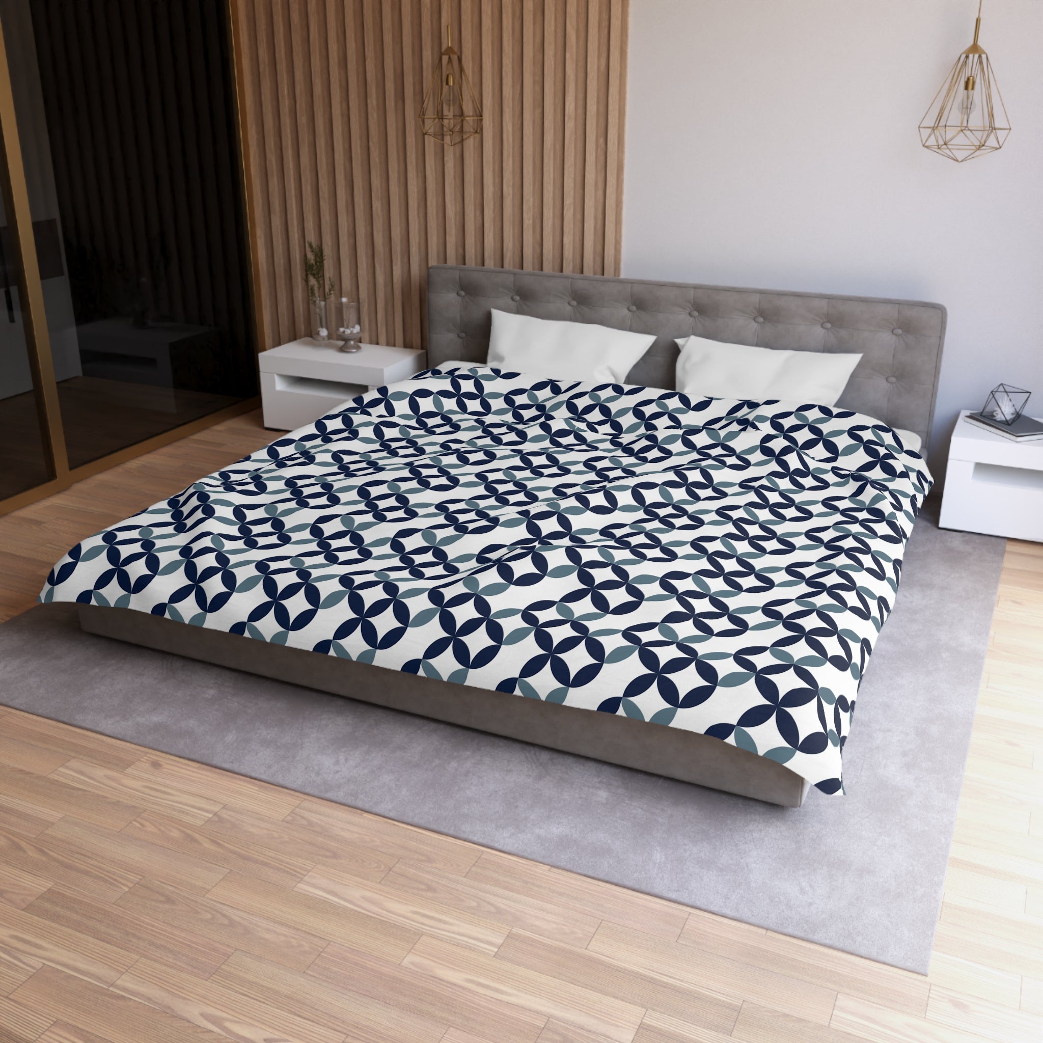 a modern bedroom with a large bed, a gray headboard, and a patterned comforter. The room has a wooden floor and white walls, creating a clean and minimalist aesthetic.