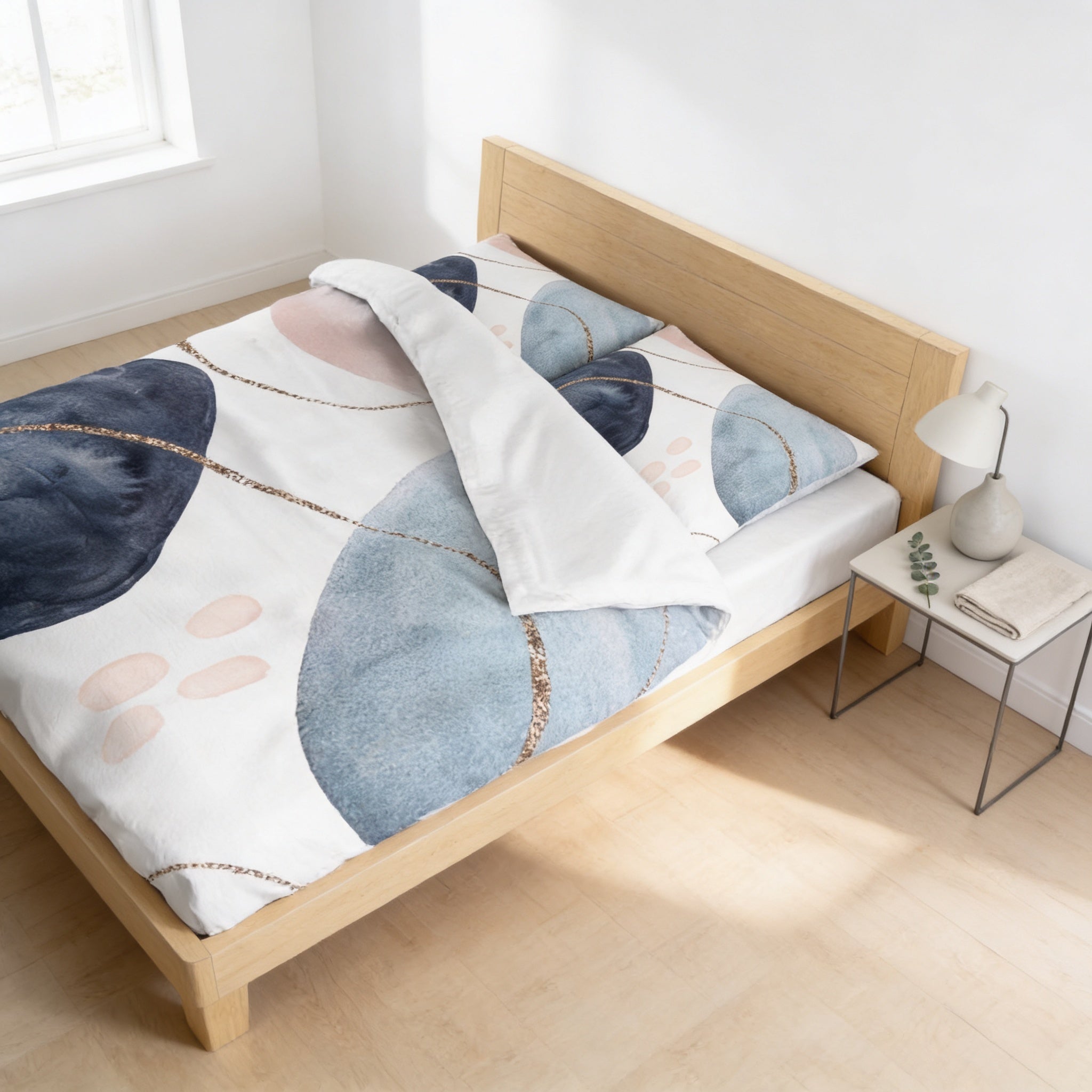 a bedroom with a bed featuring a white and blue abstract patterned comforter and matching pillow. The bed is positioned against a white wall, with a small side table next to it.