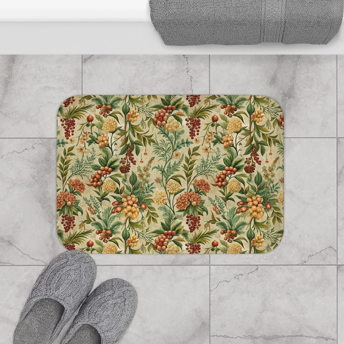 a bathroom floor with a decorative bath mat featuring a floral pattern in shades of green, yellow, and red. Next to the bath mat are a pair of gray slippers placed on the floor.