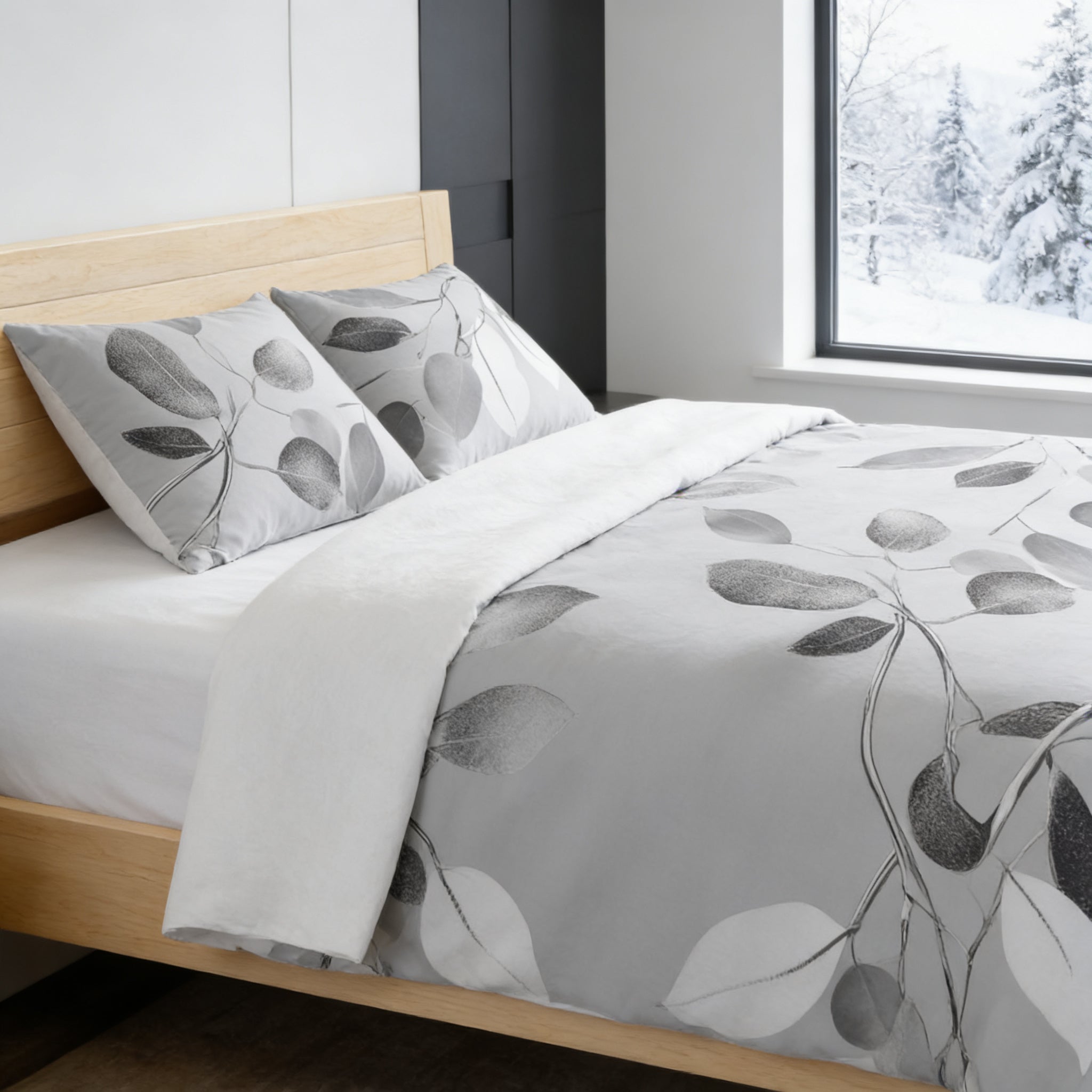 a modern bedroom with a bed featuring a gray and white leaf-patterned comforter and pillows. The bed is positioned against a wall with a window, providing a view of the snowy landscape outside.