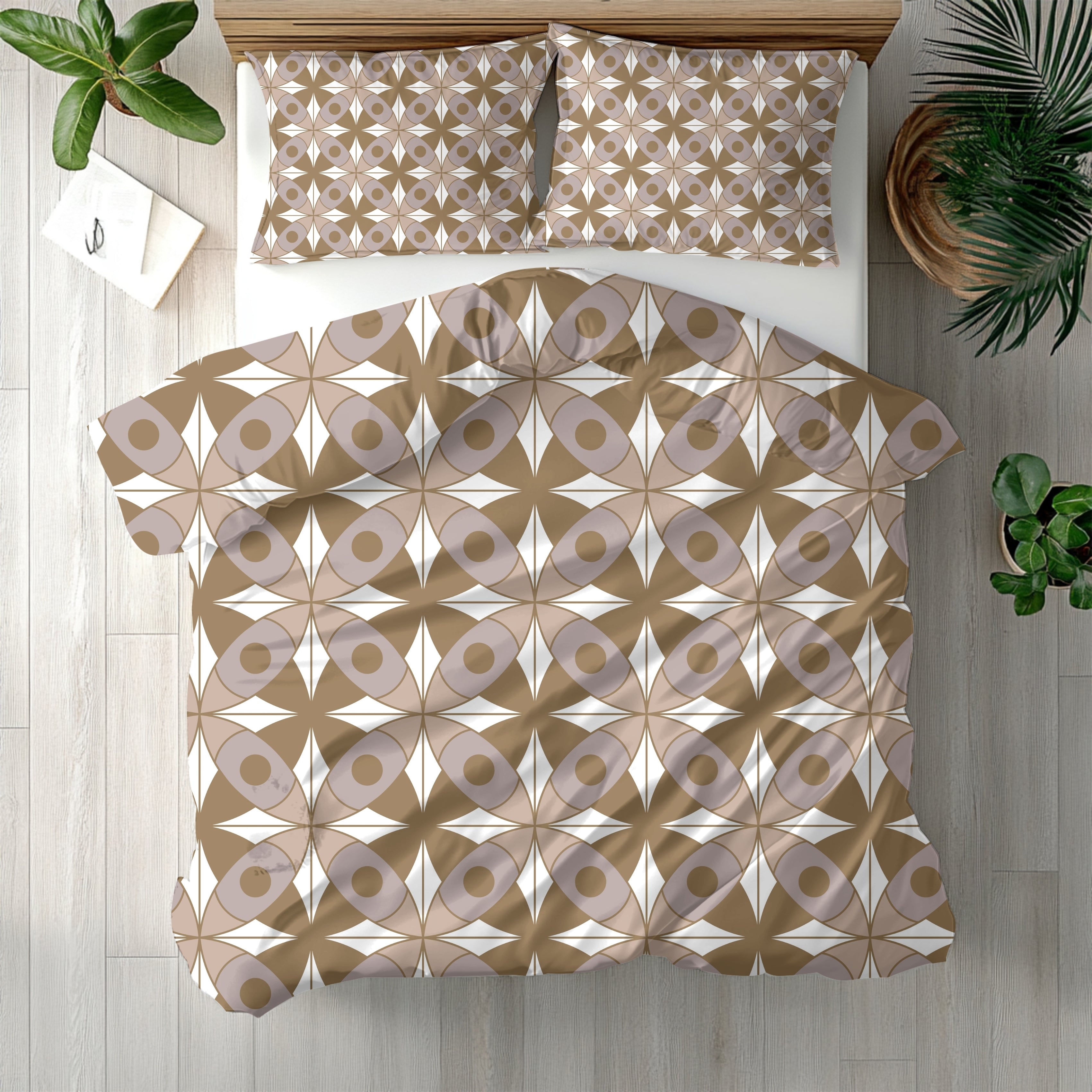 a bedroom with a bed featuring a patterned comforter and pillows. The bed is placed on a wooden floor, and there are two potted plants in the room. A book is also visible on the floor next to the bed.