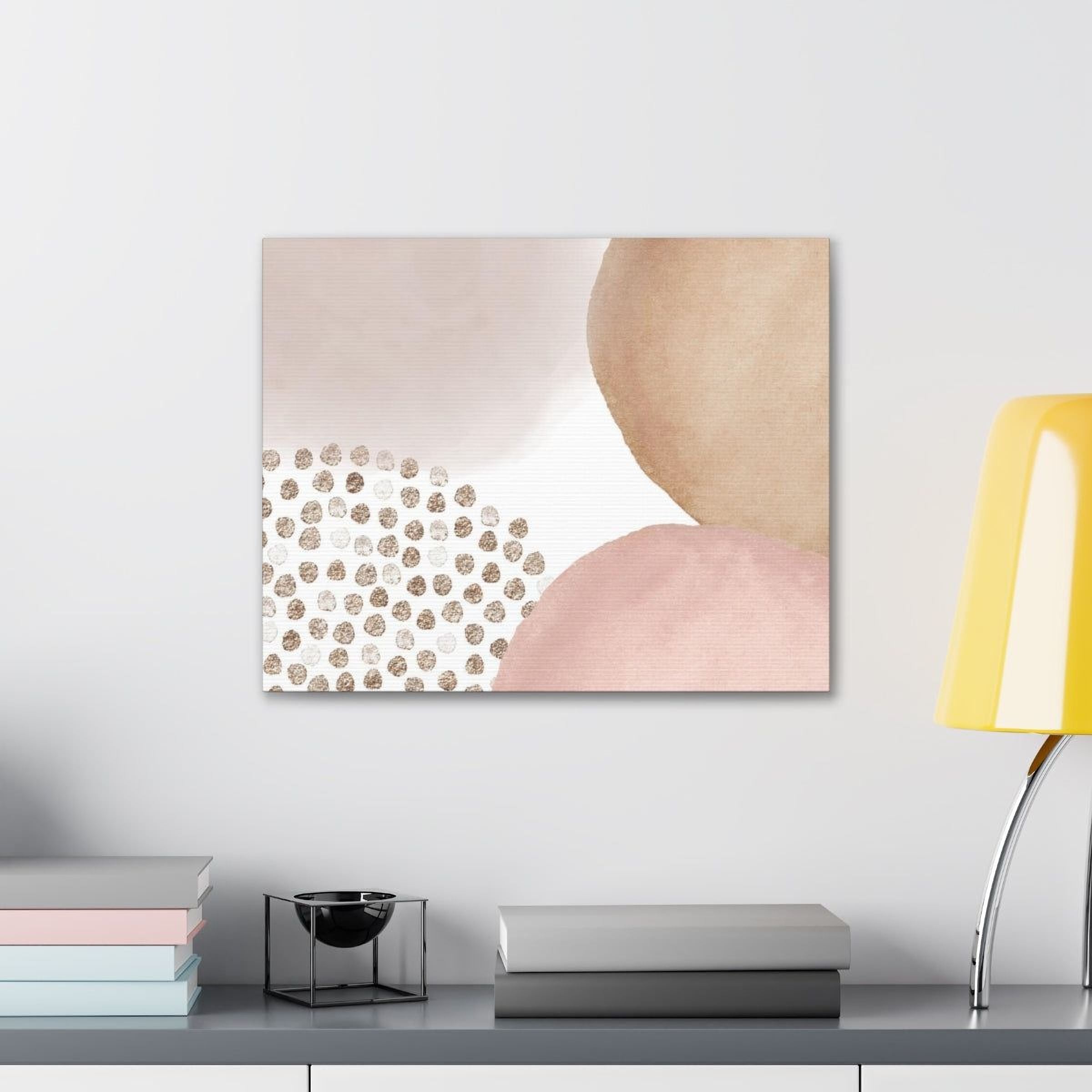 a minimalist art piece with a light pink background and scattered gold dots, hanging on a wall above a shelf with books and a small black bowl.