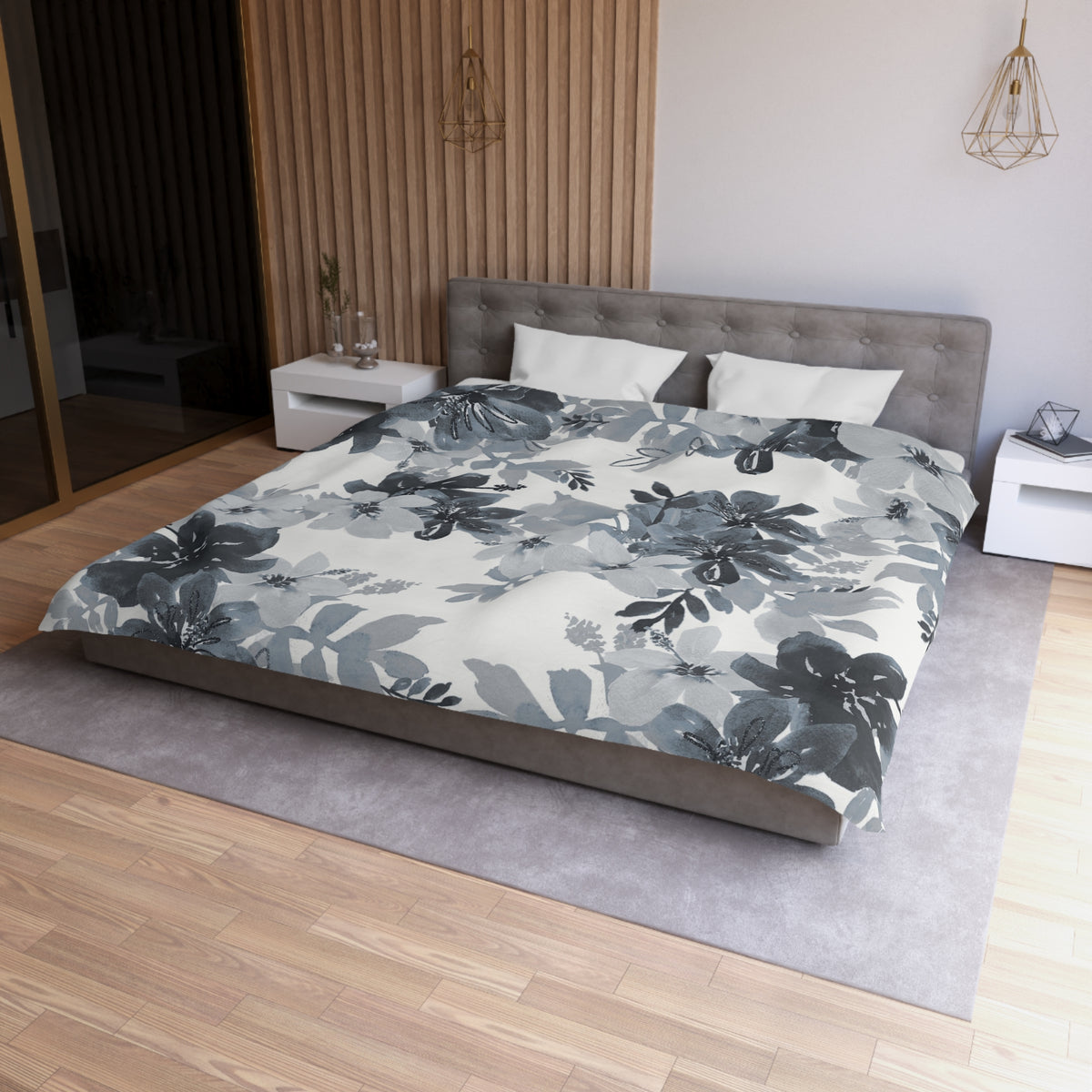 a modern bedroom with a large bed covered in a gray and white floral comforter. The bed is positioned against a wall with a wooden panel. The room also features a nightstand, a pendant light, and a rug on the floor.