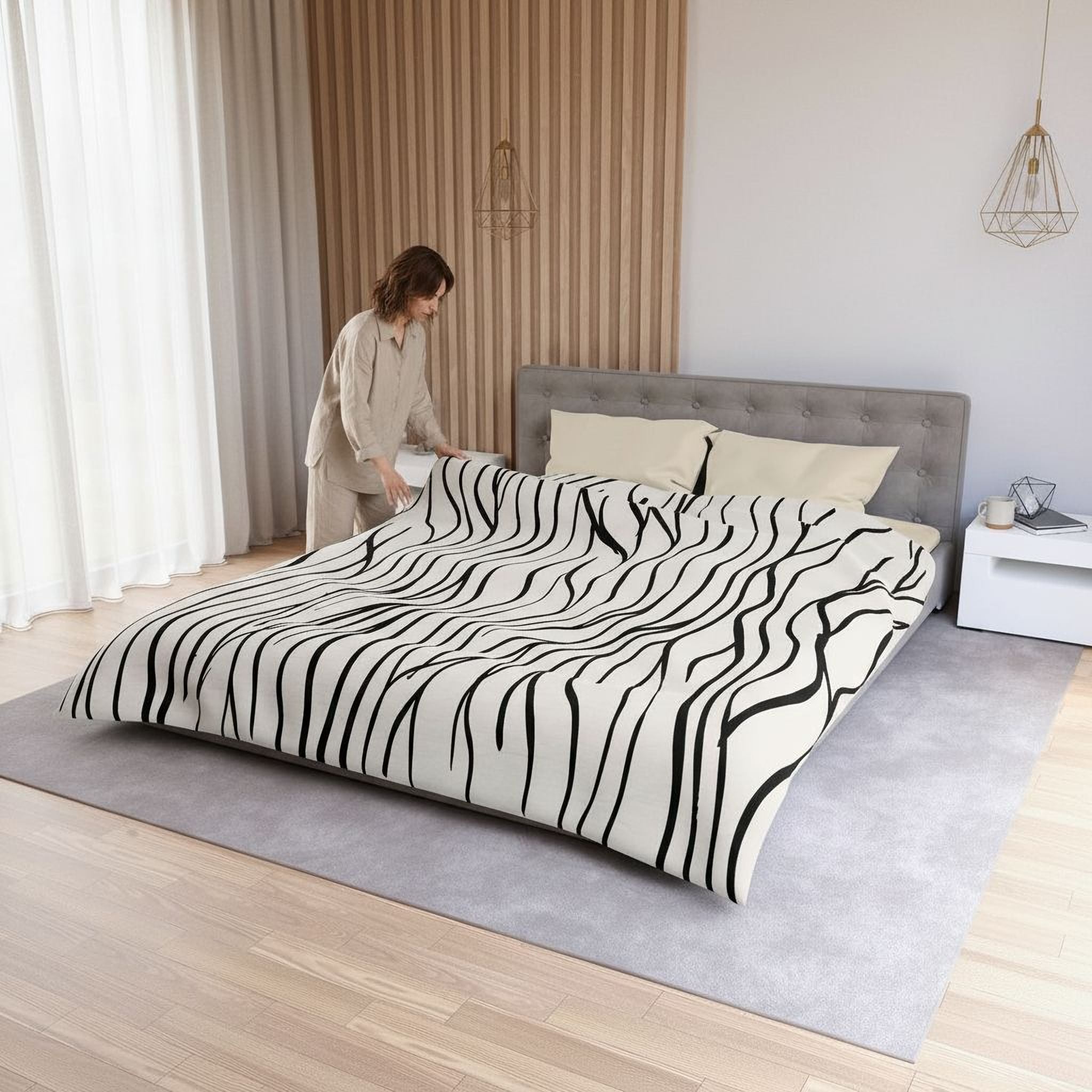 A woman is arranging a bed with a black and white zebra print comforter and pillows in a bedroom.