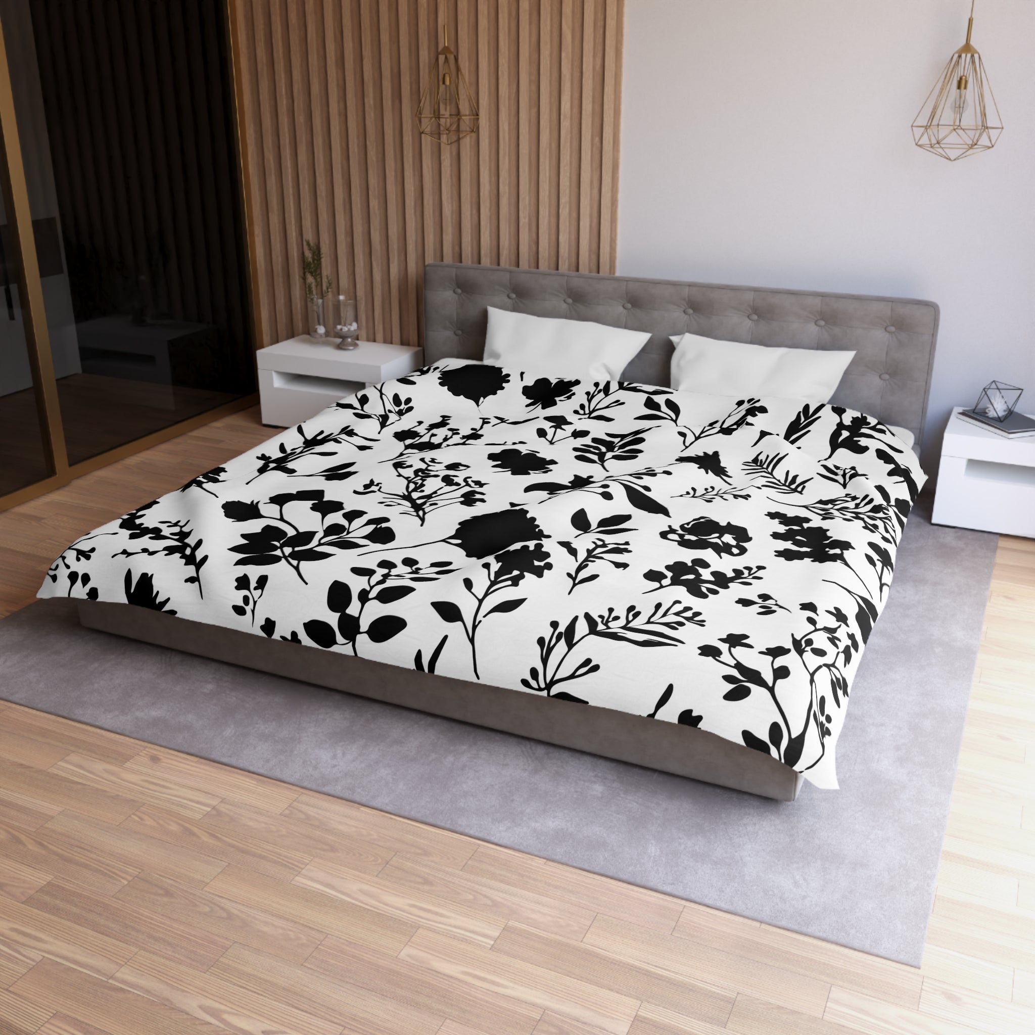 a modern bedroom with a large bed featuring a black and white floral patterned comforter and pillows. The bed is positioned against a wall with a wooden paneled accent. The room also includes a nightstand, a pendant light, and a rug on the floor.