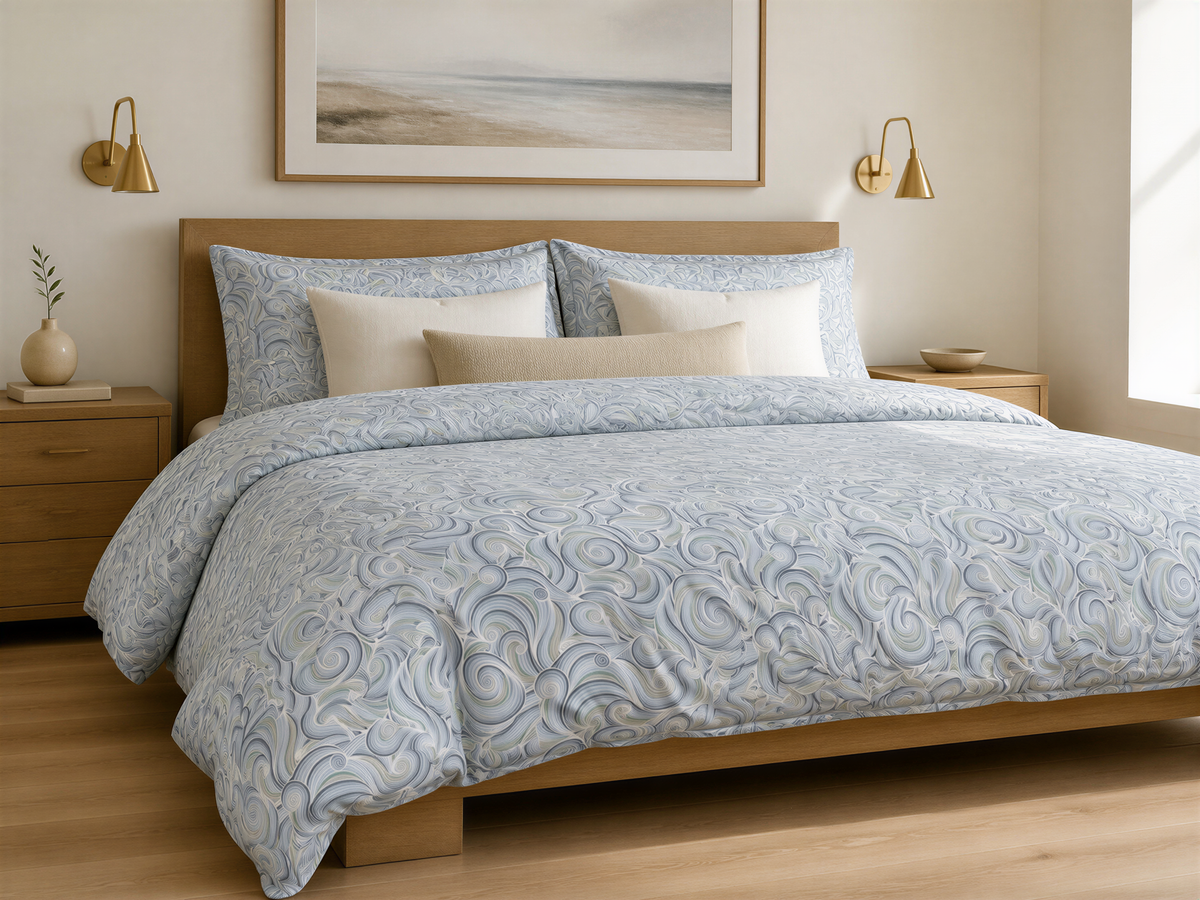 a serene bedroom scene with a large bed adorned with a blue and white patterned comforter and pillows. The bed is framed by a wooden headboard and flanked by two wall sconces. Above the bed, there is a framed landscape painting depicting a beach scene. The room has a warm, inviting atmosphere with its neutral color palette and well-organized layout.