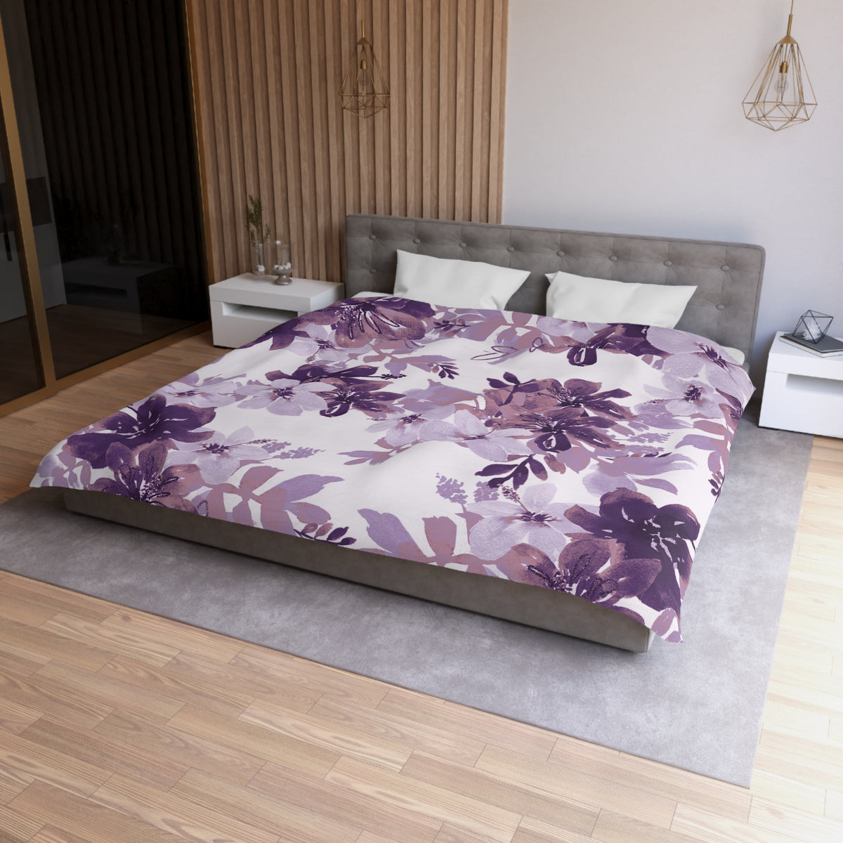 a modern bedroom with a large bed covered in a purple floral comforter. The bed is positioned against a wall with a wooden panel. The room also features a nightstand, a pendant light, and a rug on the floor.