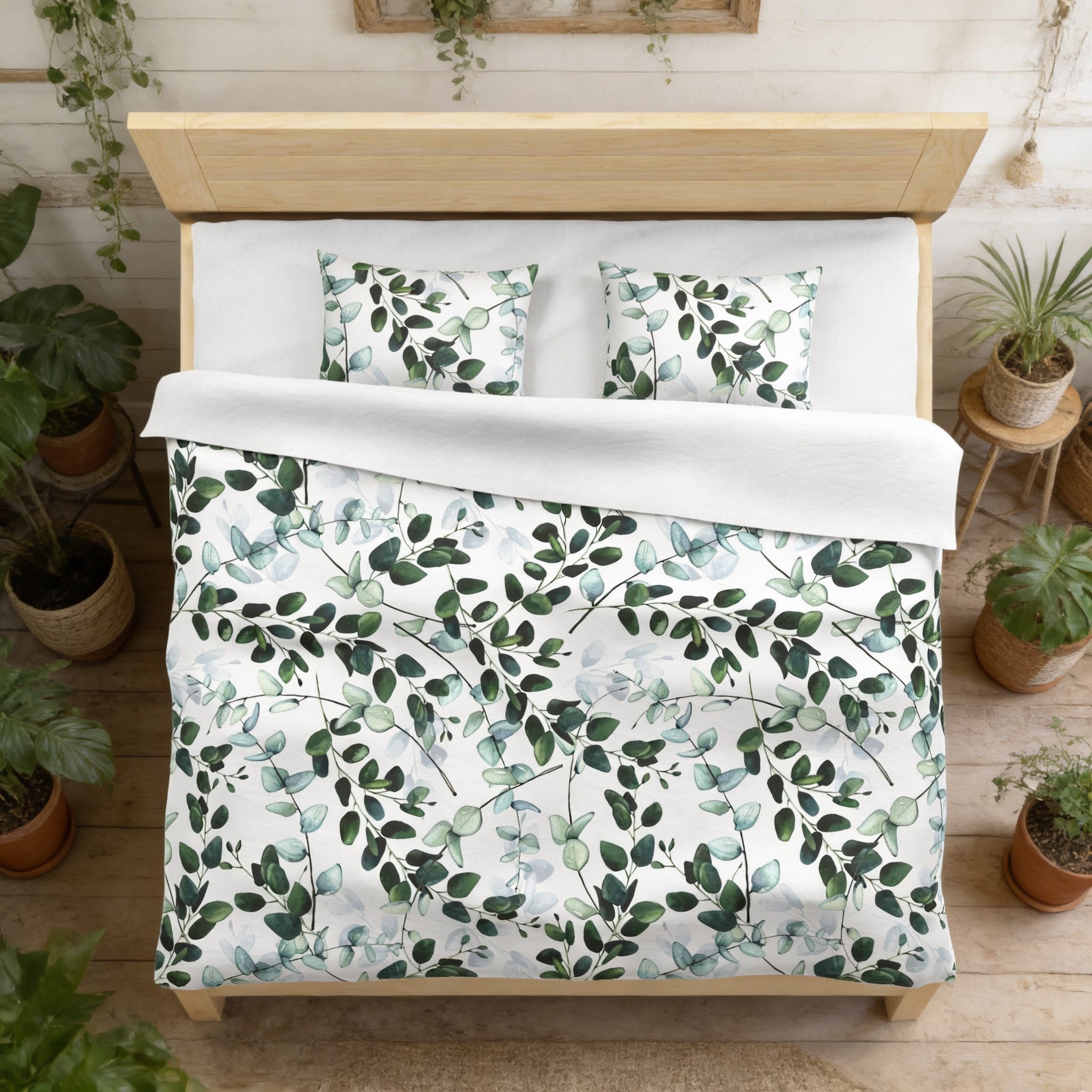 a bedroom with a bed covered in a white comforter and pillows, featuring a leafy green and white pattern. The bed is surrounded by potted plants, creating a cozy and natural atmosphere.