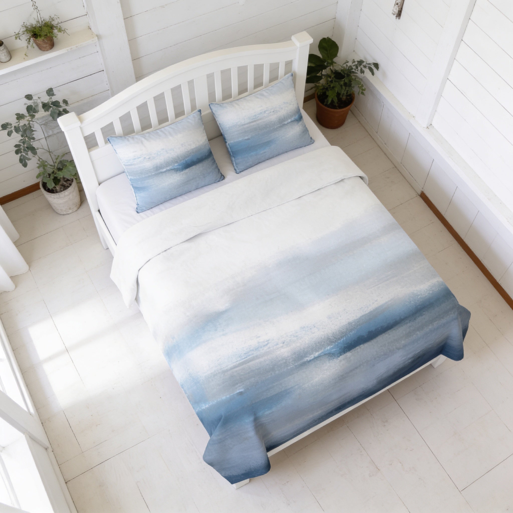 a white wooden bed with a blue and white patterned comforter and pillows, placed in a bright and airy room with white walls and a wooden floor.