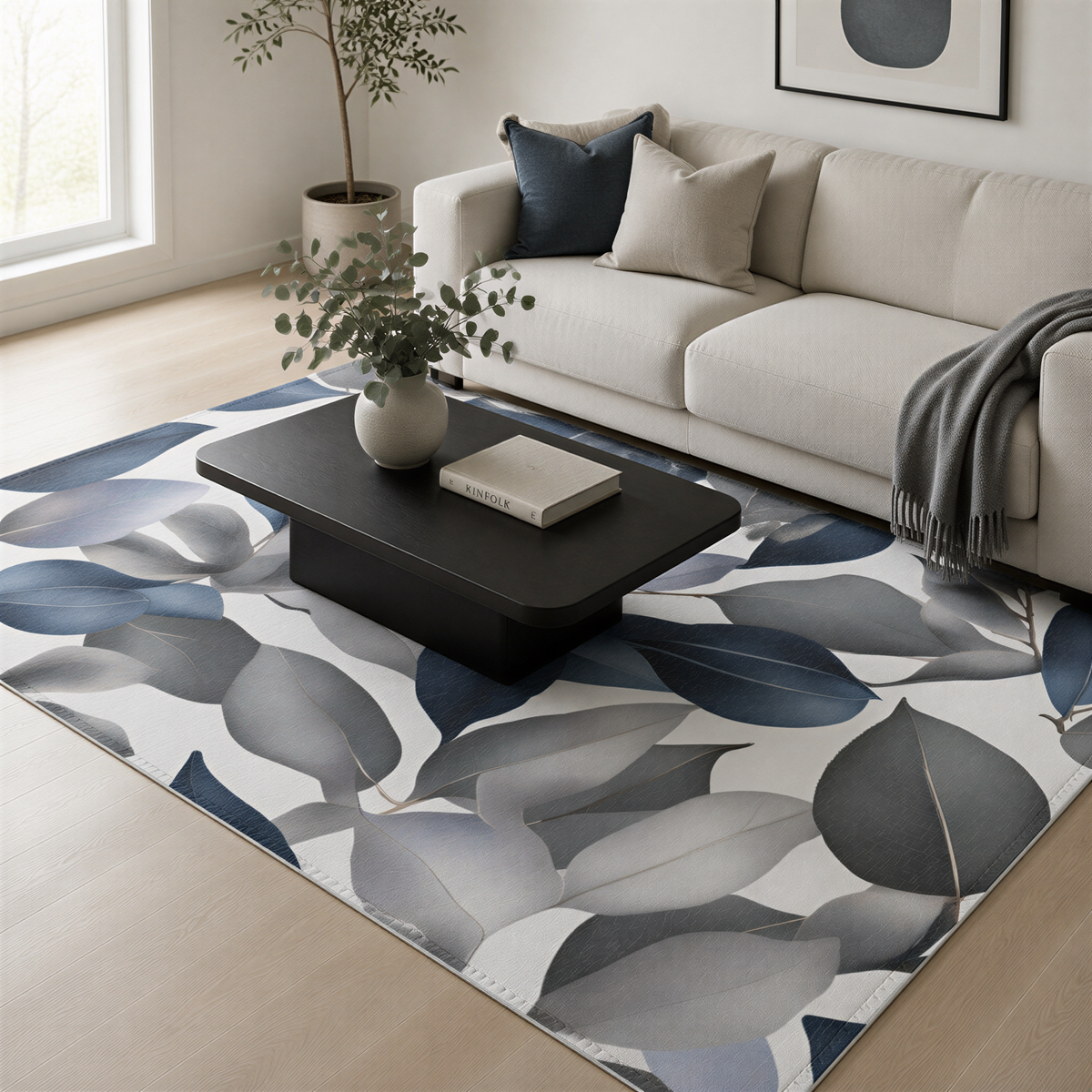 a modern living room with a white sofa, a black coffee table, and a large area rug with a leaf pattern. The room is decorated with a potted plant, a book, and a gray blanket.