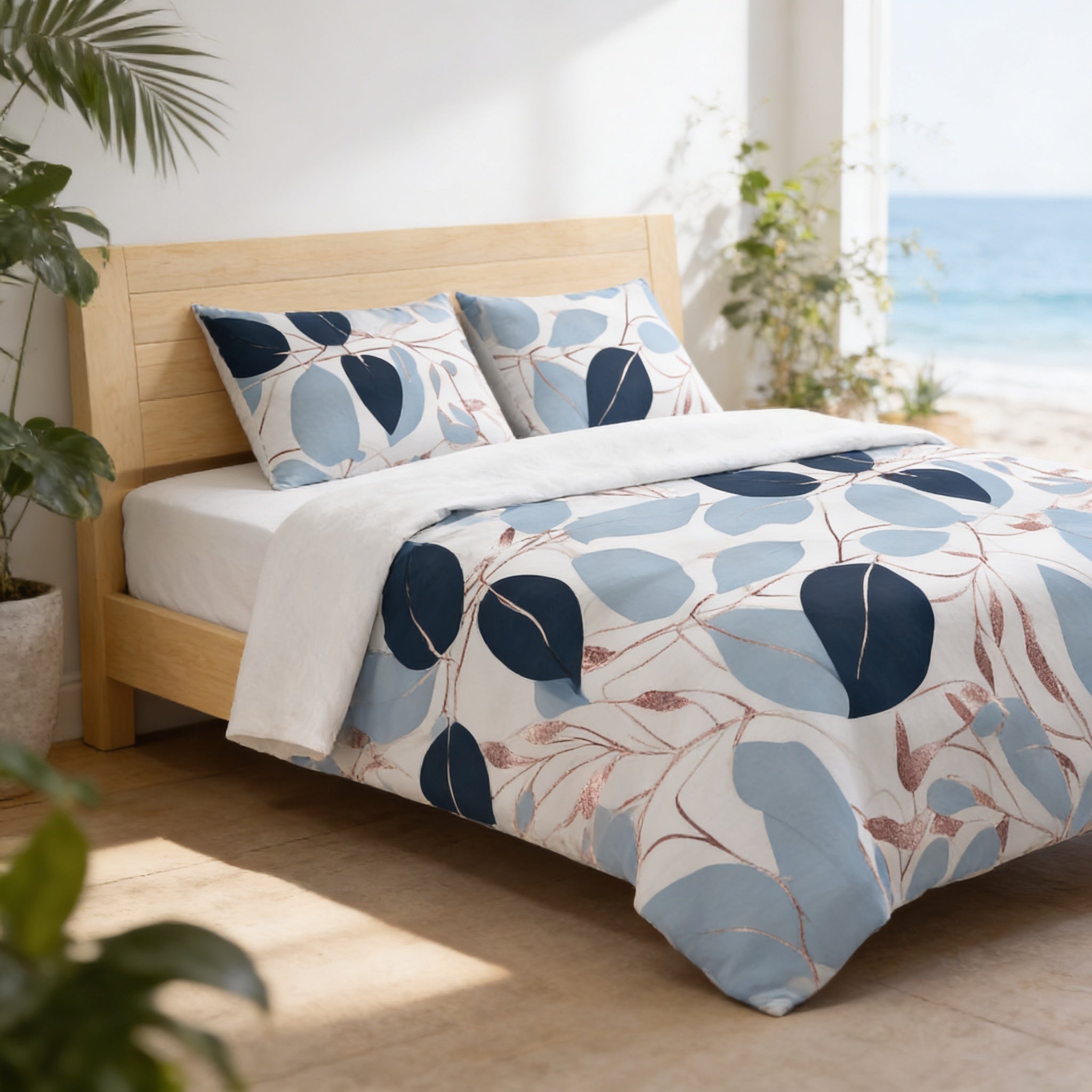 a bedroom with a bed featuring a blue and white leaf-patterned comforter and pillows. The bed is positioned against a wall with a window overlooking the ocean. The room has a minimalist and serene atmosphere, with potted plants and a view of the beach visible.