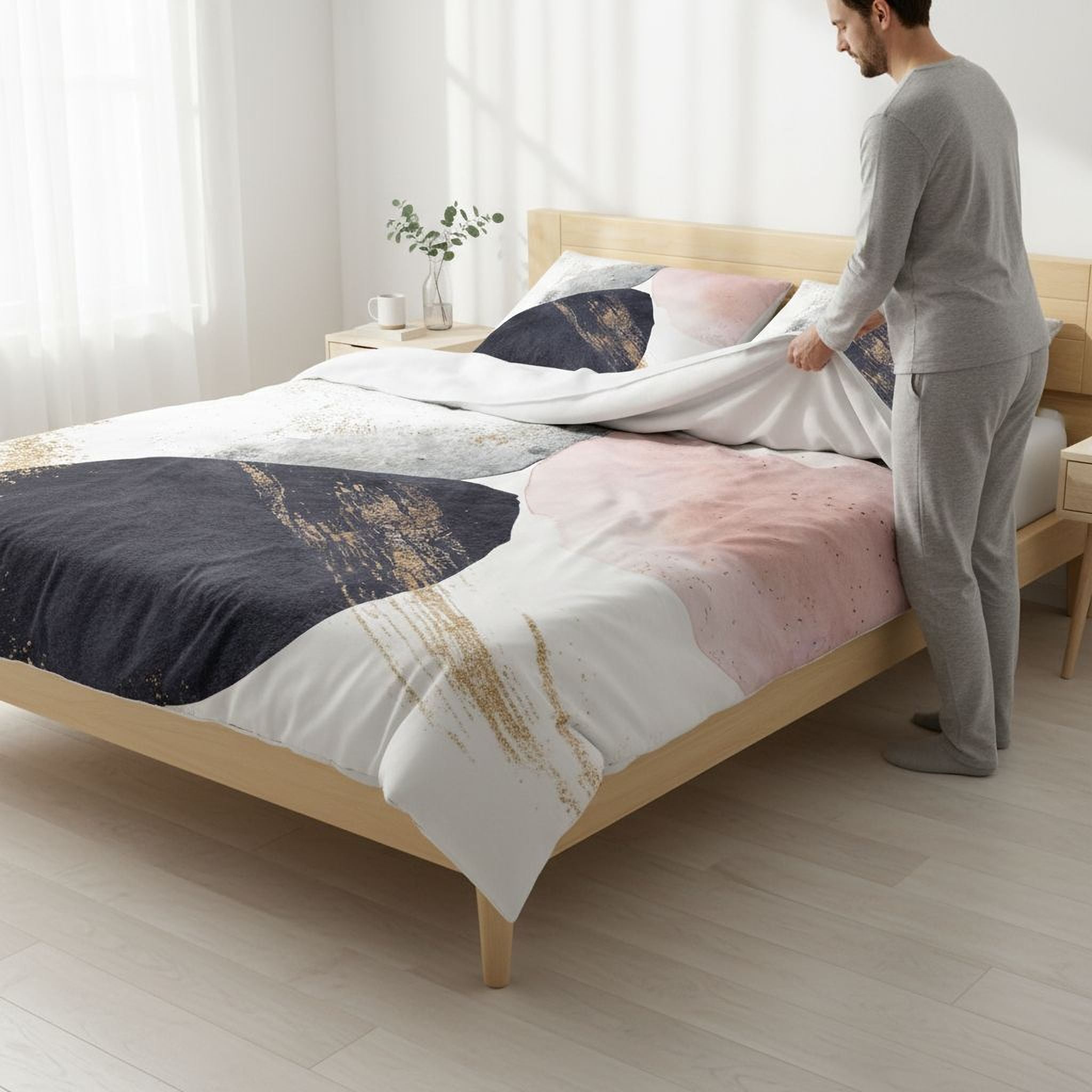 A man is standing in a bedroom, preparing a bed with a colorful, abstract-patterned comforter and pillowcases.