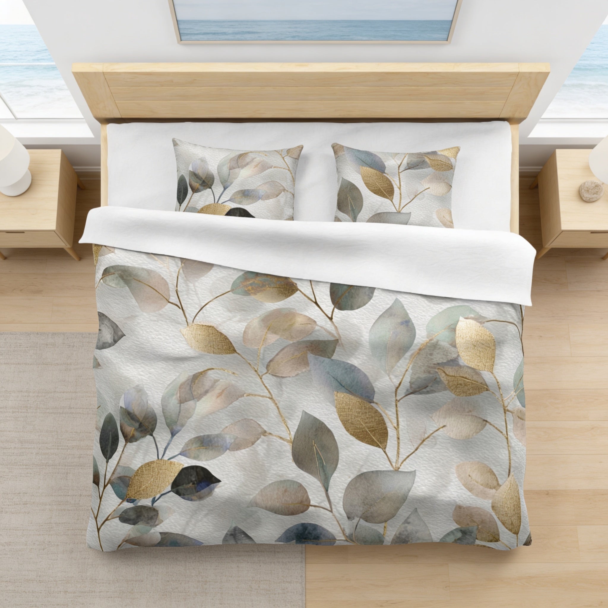 a bedroom with a bed covered in a white comforter and pillows, featuring a leaf-patterned design in shades of gray, green, and brown. The bed is positioned against a wall with a window overlooking the ocean, creating a serene and natural atmosphere.
